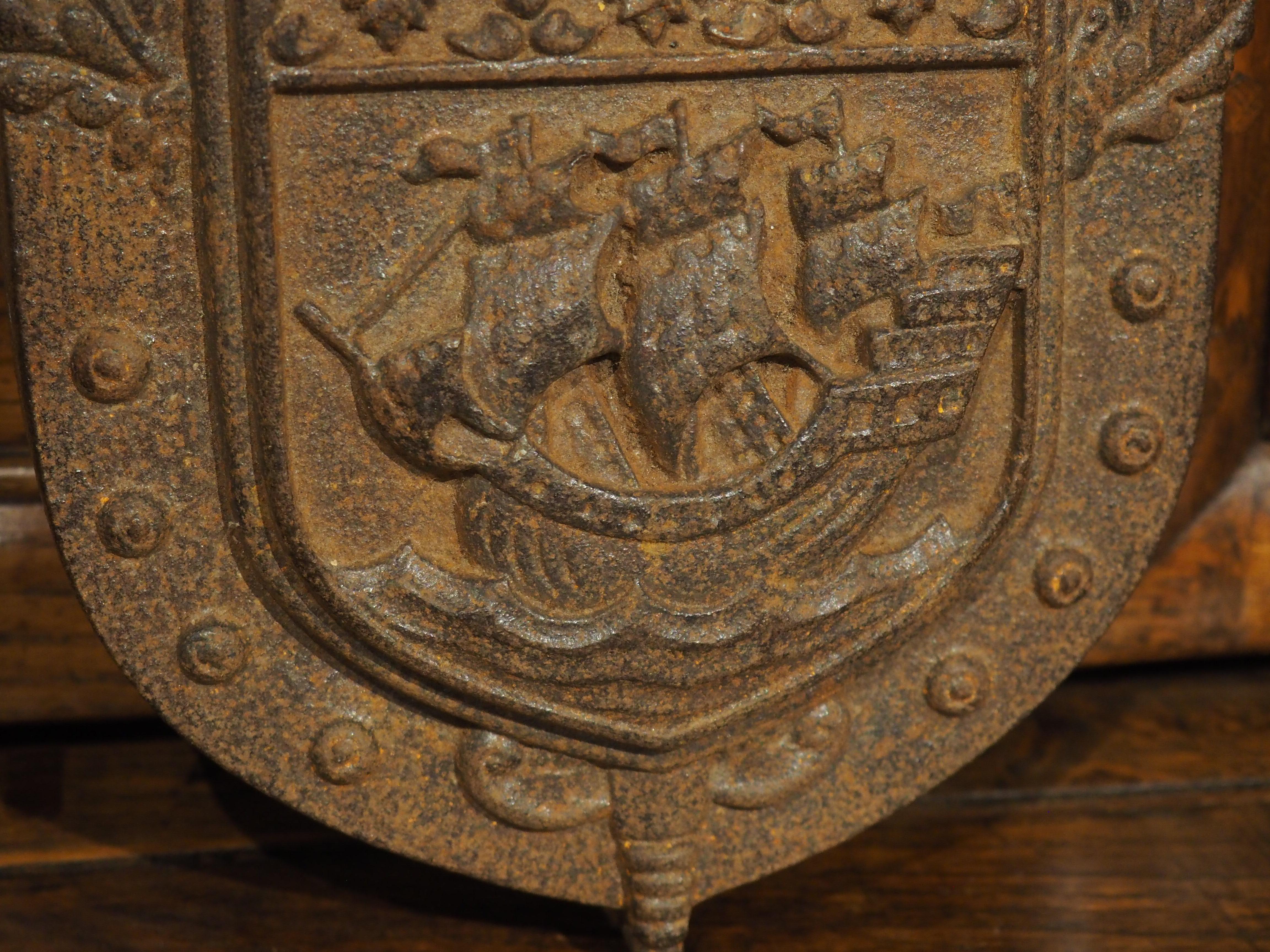 With its thick relief elements, this small cast iron wall plaque depicts the coat of arms of Paris beneath a plumed great helm. Dating to the 1900s, the plaque has a deep brown finish with some areas containing orange oxidation. The knight helmet is