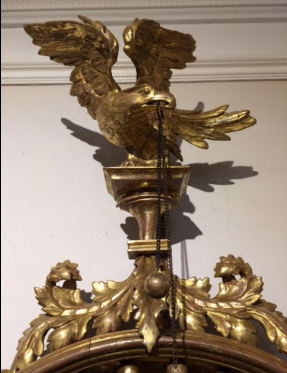 Petit miroir convexe doré et sculpté de la période Régence, cadre décoratif mouluré rehaussé de sphères dorées appliquées et d'une bordure perlée, engobe ébène à l'intérieur, surmonté d'un aigle finement sculpté tenant une boule et des chaînes dans