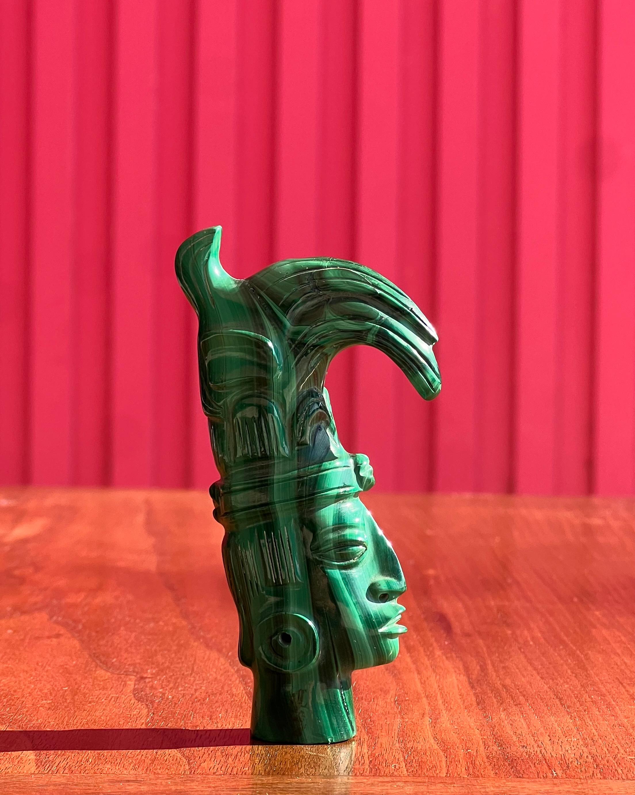 A hand-carved malachite sculpture depicting an indigenous tribesman - possibly Mayan or Aztec - , probably 20th century. A hole is carved on verso bottom of sculpture so he can be fit into a rod on plinth, but he also stands up without.