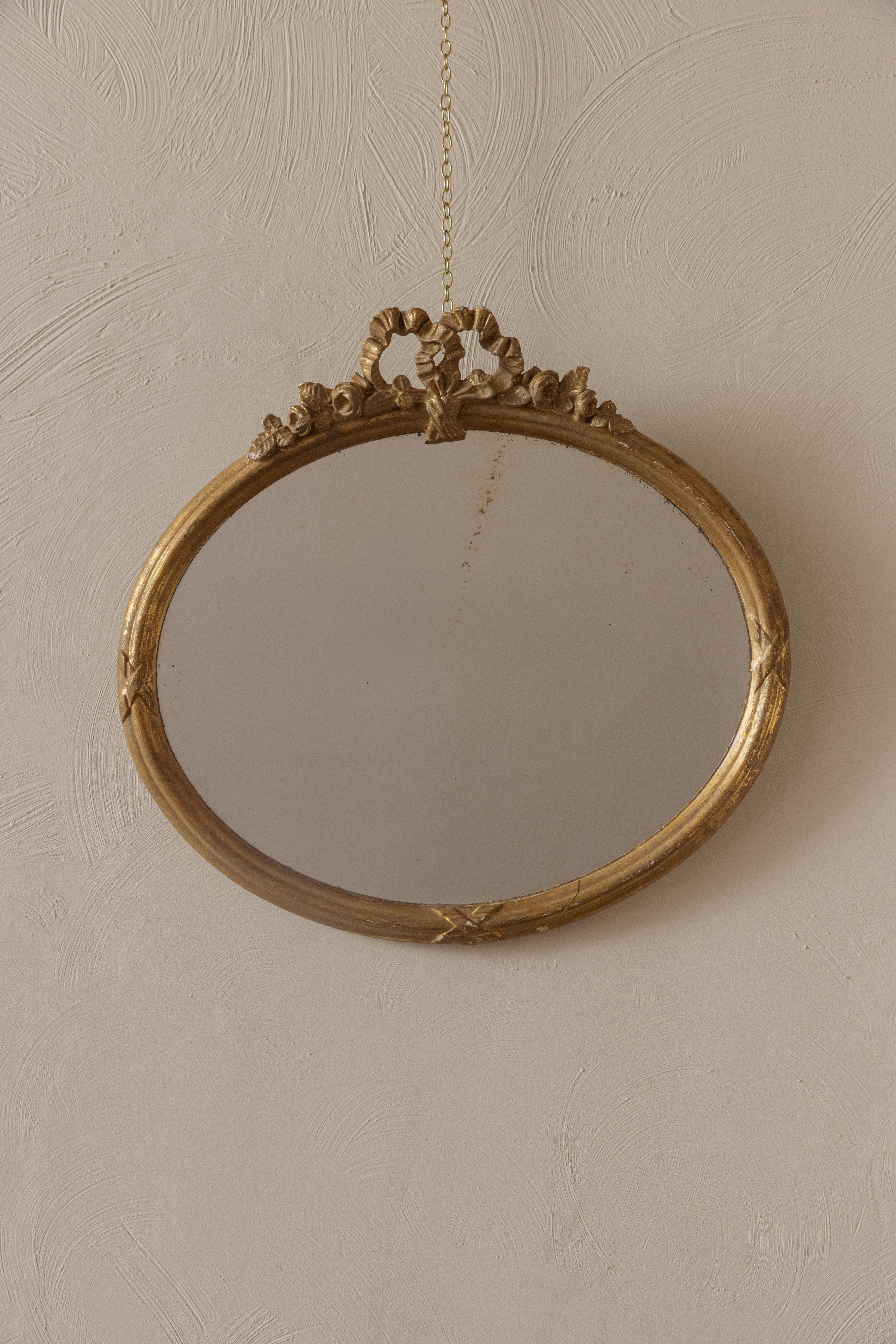 A very pretty gilt oval mirror with floral and ribbon motifs crest in the Rococo style. Likely to come from France. Perfect for above a basin. Original glass - shown by the slight foxing.