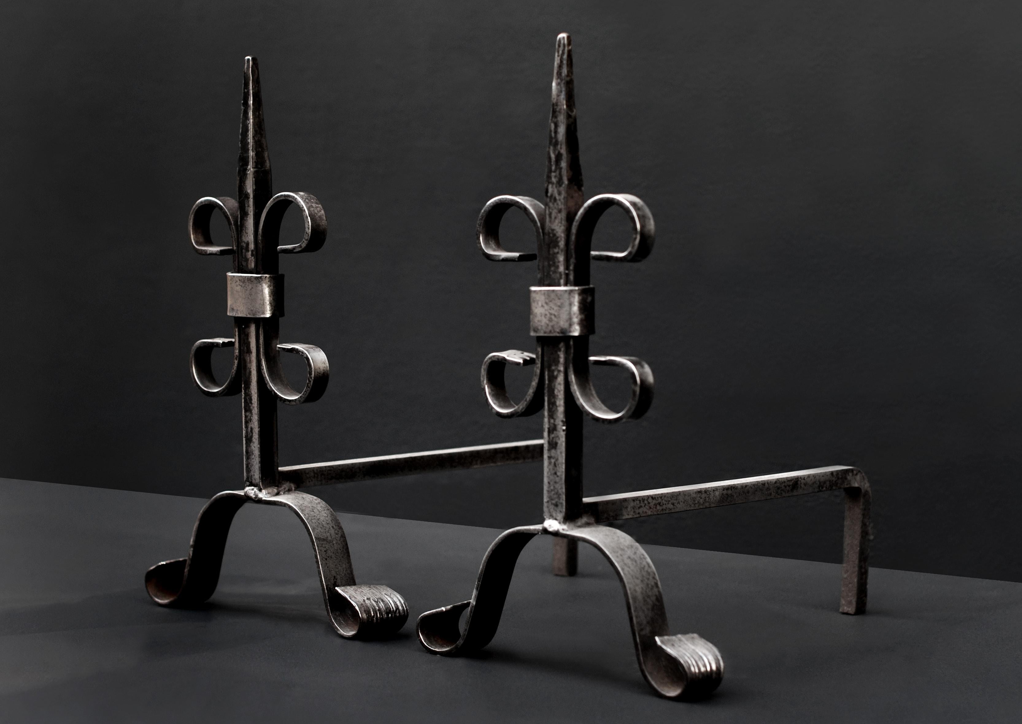 A pair of English polished wrought iron firedogs in the Gothic style. 20th century. (Back bars could be extended if required).

Measures: Height: 395 mm 15 ½