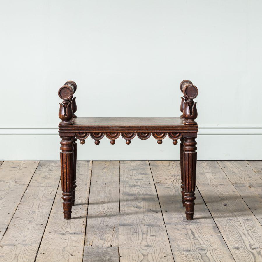 With turned bolster lotus leaf supports, above a panelled seat with a frieze of half roundels and ball pendants, on turned fluted legs, circa 1815.