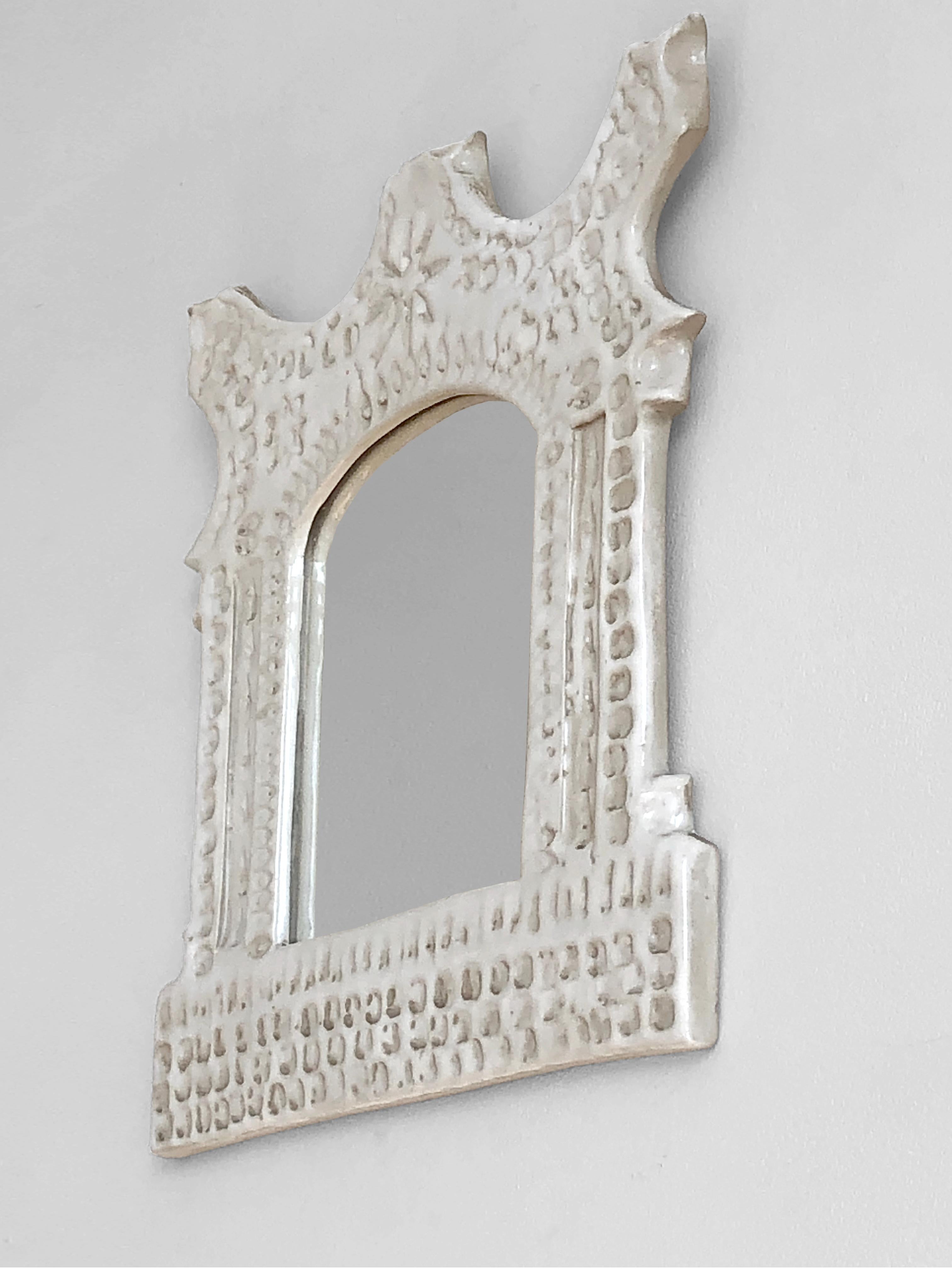 Ein skulpturaler, kleiner und eleganter Wandspiegel,  breiter Freiformrahmen mit geritzten Reliefs, milchig-weiß emaillierte Keramik, von noch unbekanntem Künstler,  aus Vallauris, Frankreich 1970.