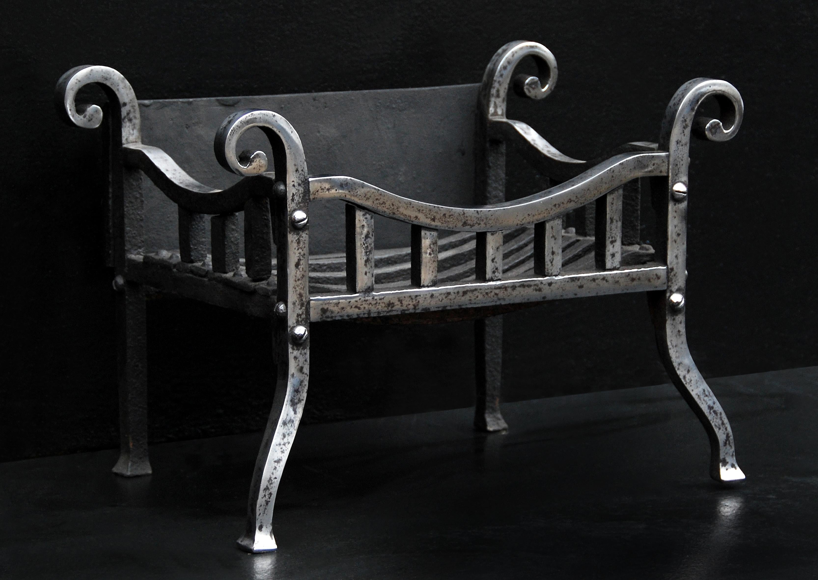 A small scrolled firegrate in the Arts & Crafts manner. The shaped legs surmounted by square uprights and bowed top bar. Scrolled finials to front and rear. Antiqued finish. Modern.

Width At Front:	600 mm      	23 ⅝
