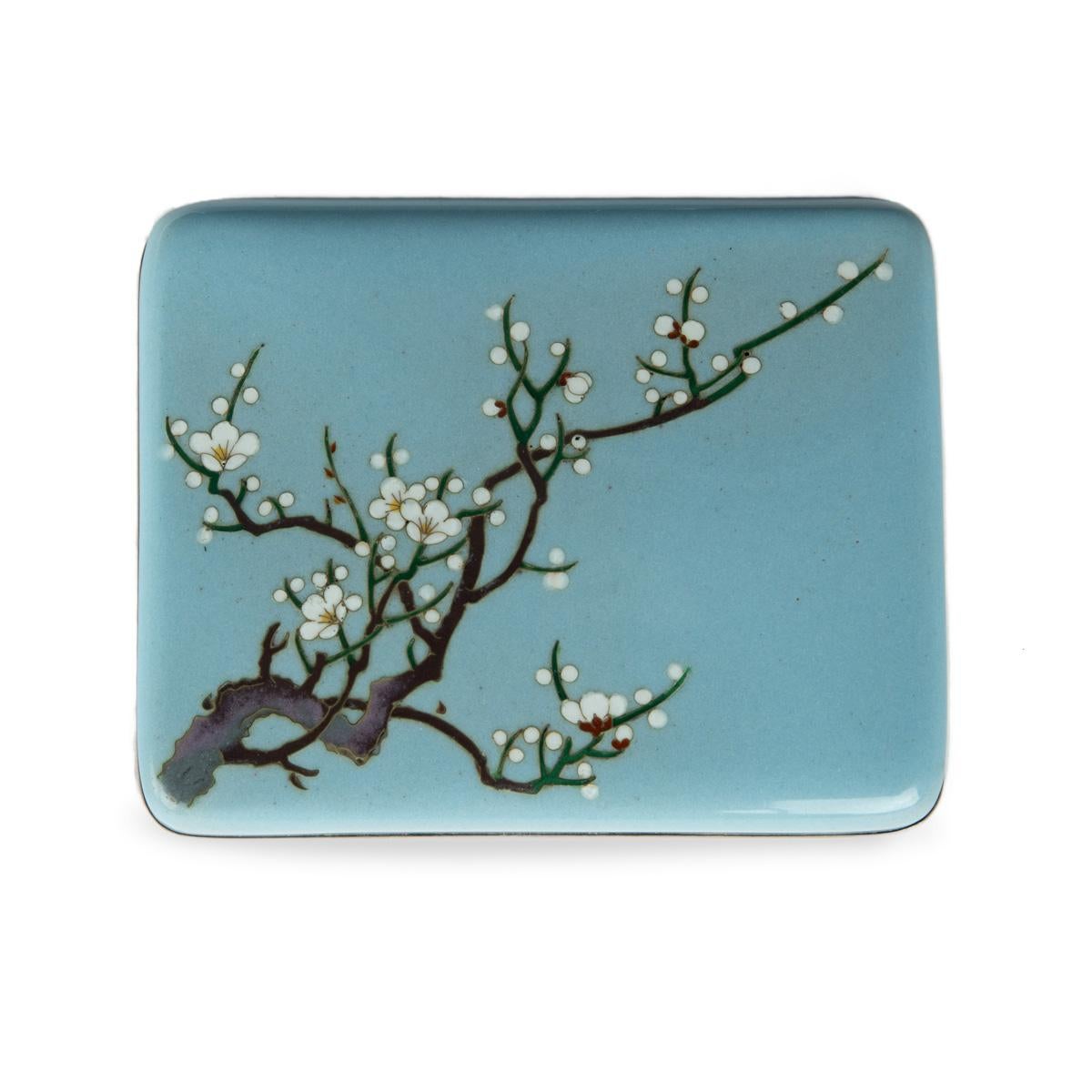 A small Showa period cloisonné box with a single branch of blossom, worked in wire and coloured enamels with a blossoming plum branch, reserved against a pale-blue ground, with silver rims and a silk lining.  Japanese, circa 1960.

