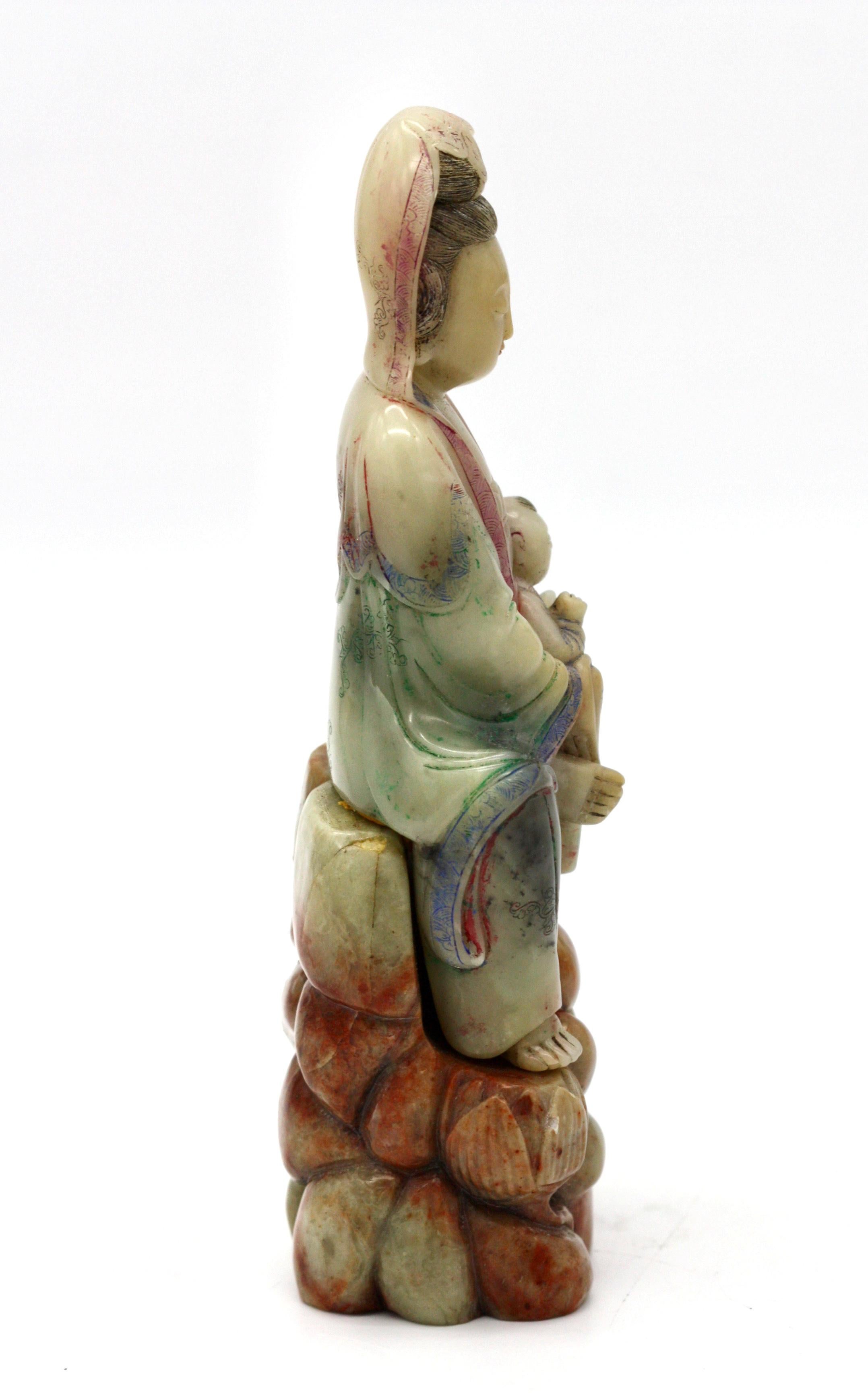 Eine Specksteinfigur von Songzi Guanyin
in lalitasana sitzend, mit beiden Händen einen Knaben auf dem Knie wiegend, bekleidet mit einem Gewand, das mit Wolkenrollen beschriftet ist, an der Brust offen ist und in dicken Falten über den Körper fällt,