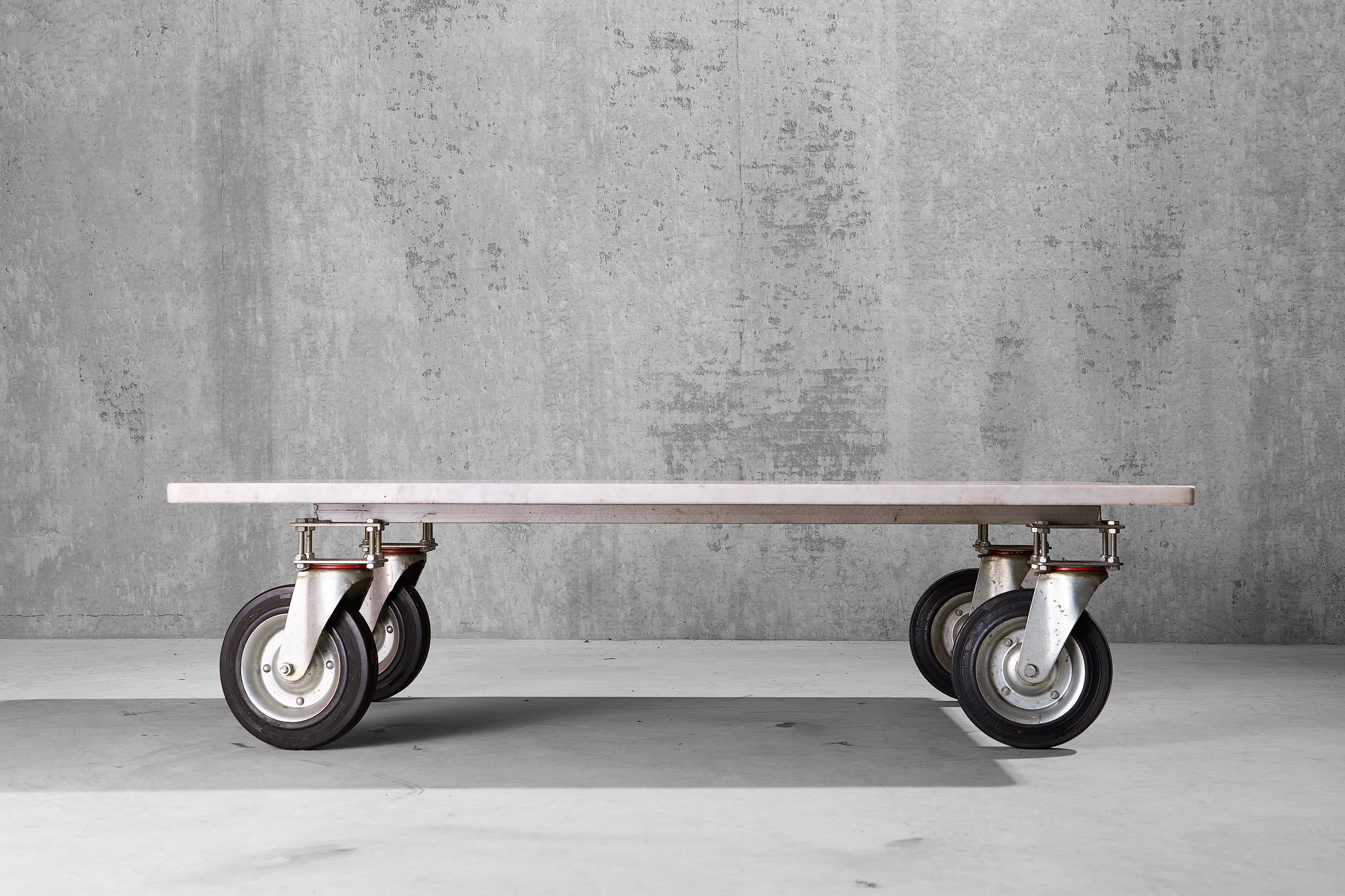 A solid industrial style modern coffee table with a white Carrara marble top on four wheels. 