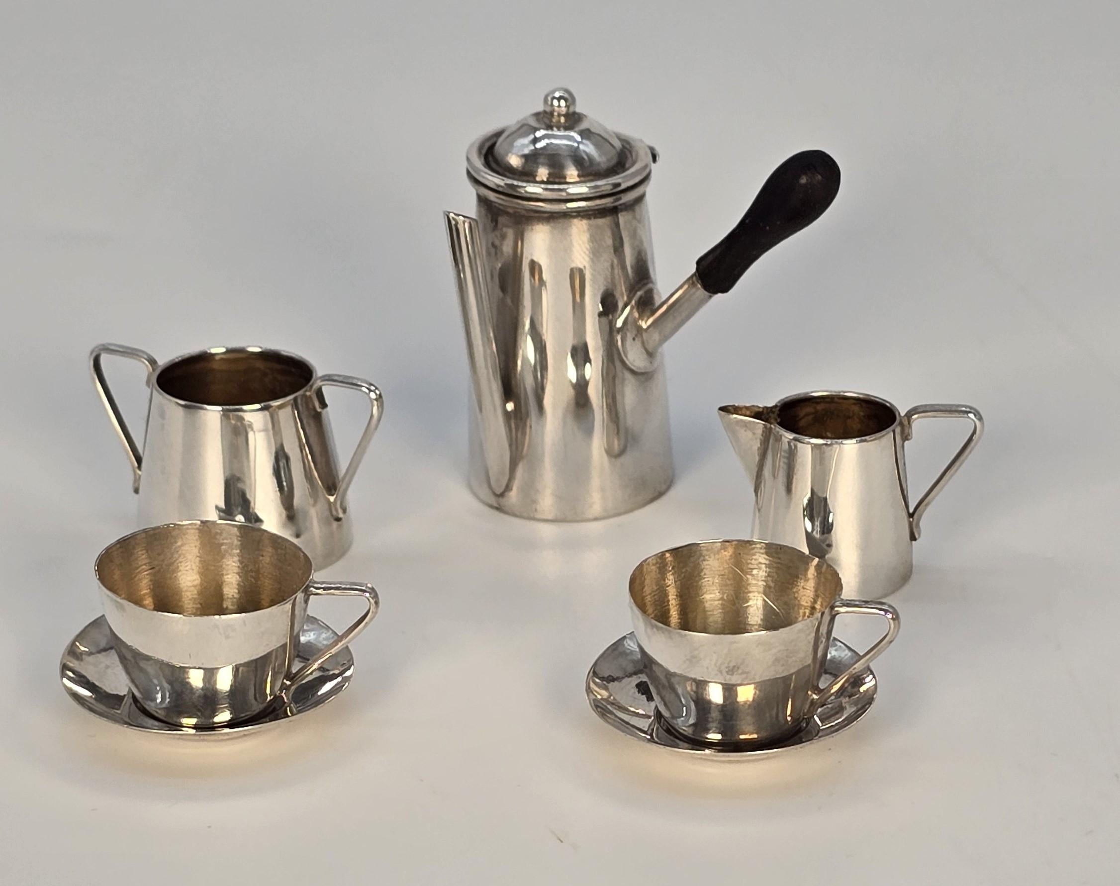 This very rare and fine-quality Edwardian miniature solid silver chocolate pot set consists of two matching cups and saucers, a cream jug, a sugar basin, and a superb chocolate pot with a hinged lid and a turned ebony side handle.

All of the pieces