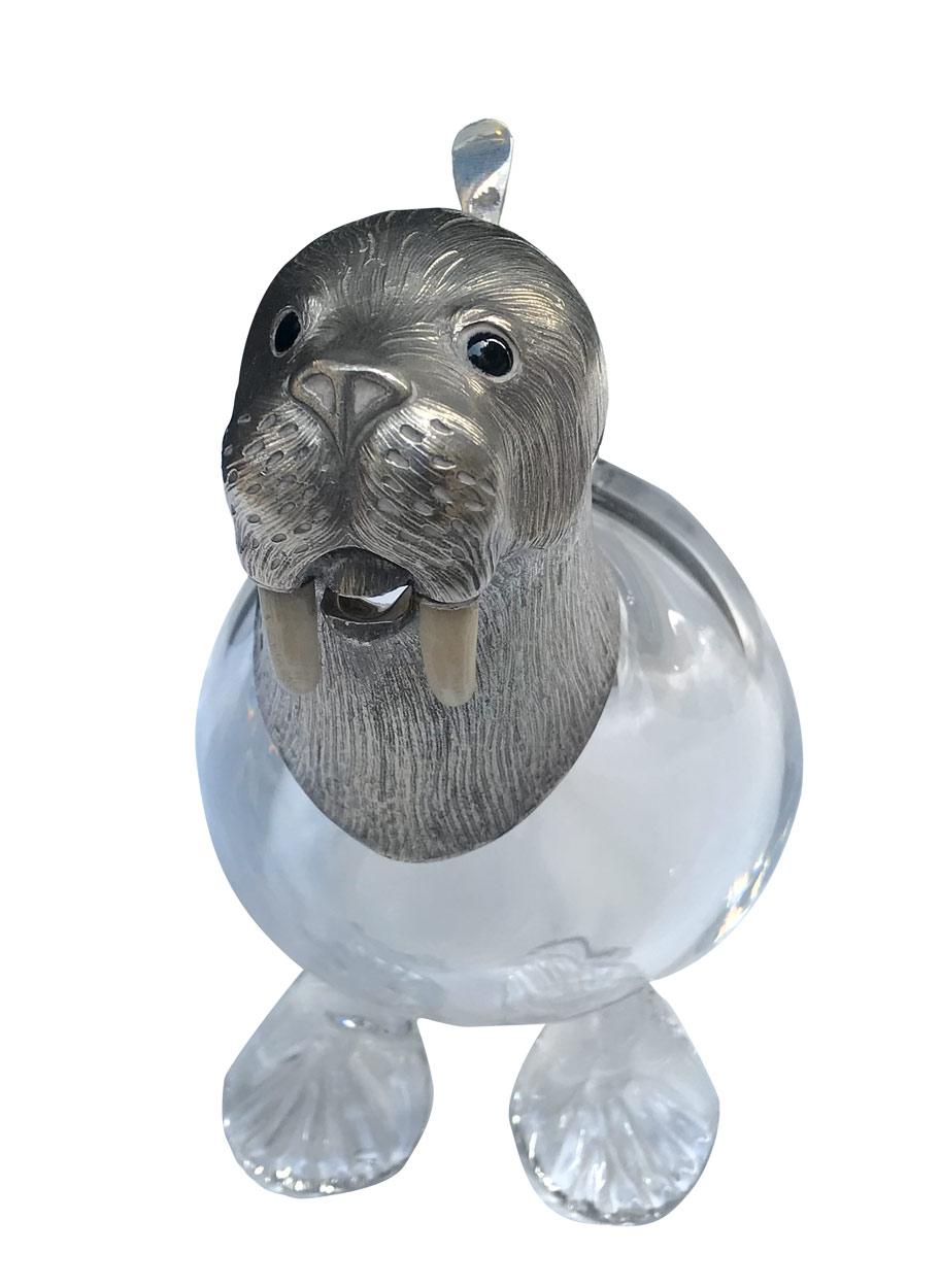 A luxury silver-mounted claret jug with glass in the shape of a walrus. Victorian style item, with precise and realistically detailed head. 
Jug with a glass handle on the back of the walrus; the hinged head is forming a lid. Inspired by the famous