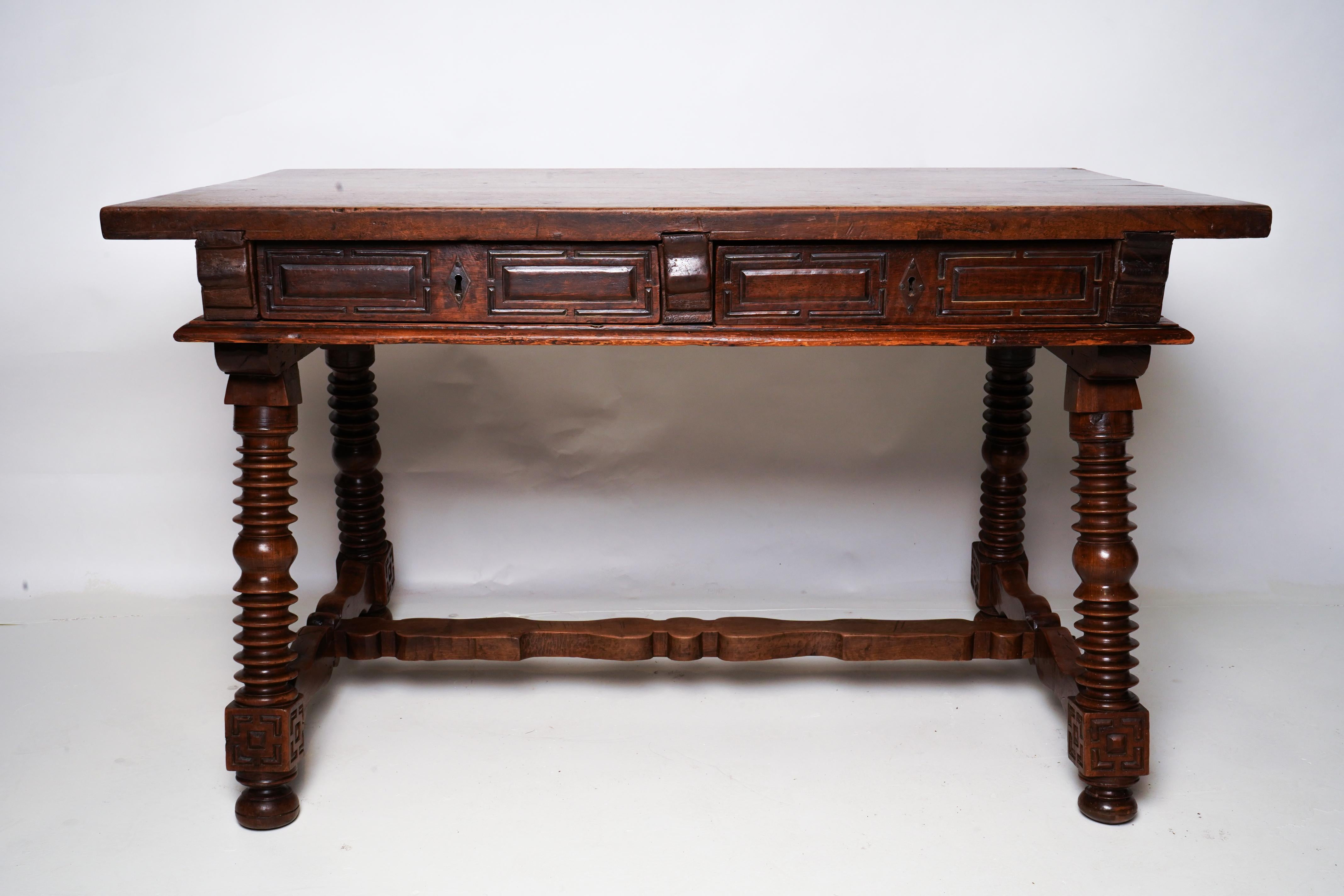 An 18th century Spanish baroque desk, or writing table made of solid Walnut Wood with turned legs joined by a Two drawers with original iron drawer pulls and two false drawers in back. The top is made from two planks of Walnut held together by 3