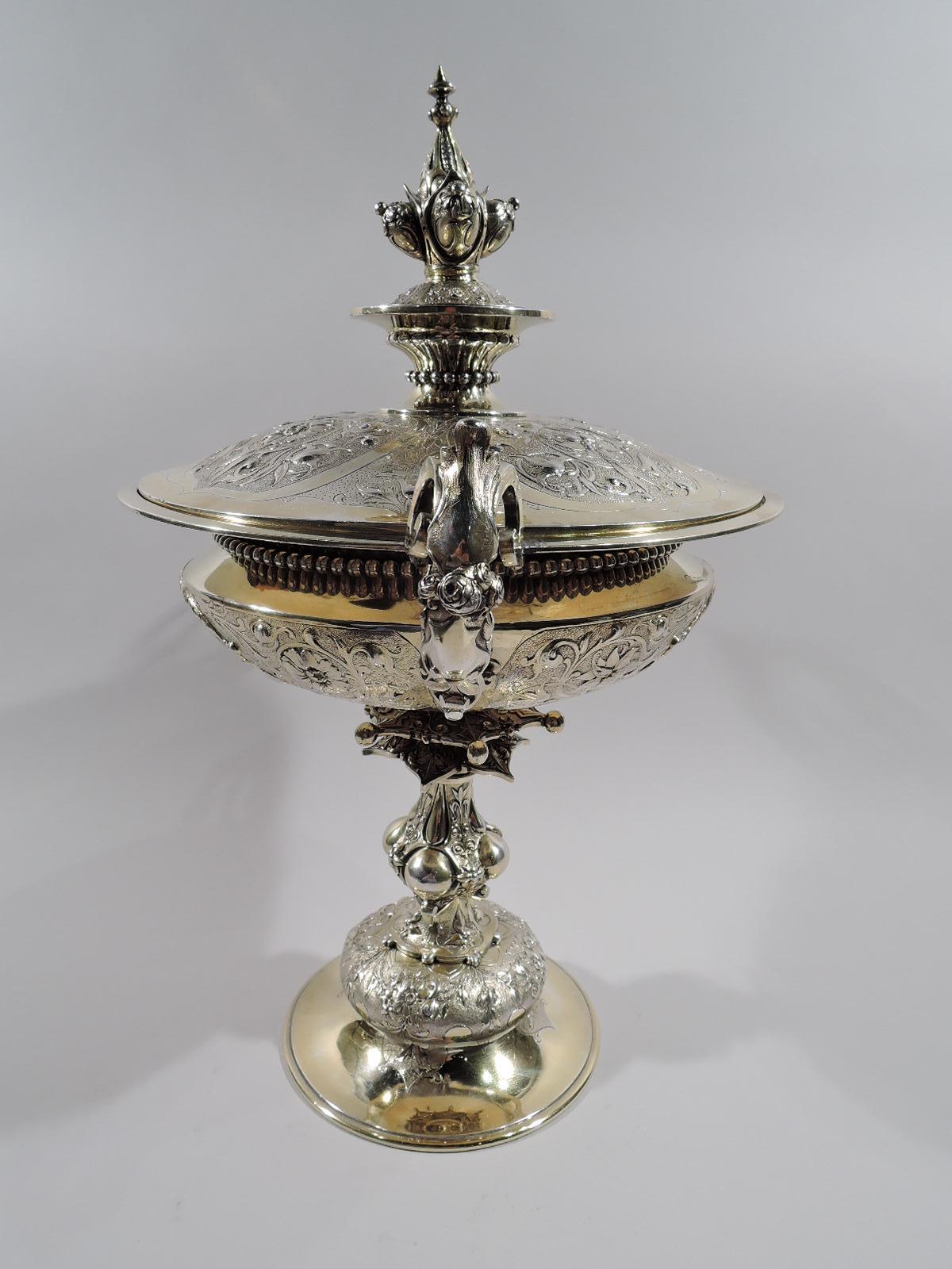 A souvenir of Raj India: English gilt sterling silver covered trophy cup, 1863. Bellied bowl with leaf-mounted and capped C-scroll handles with split C-scroll mounts. Baluster shaft with two star-flanges on dome with chased naturalistic flowers in