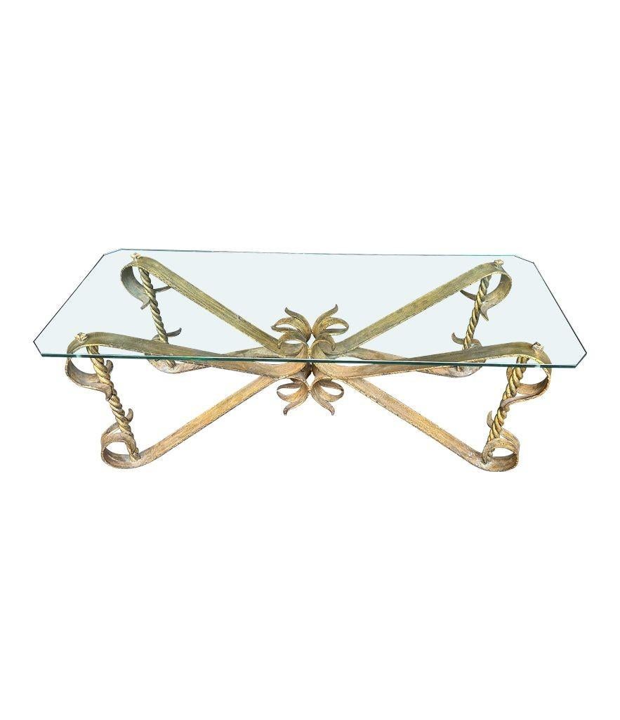 Table basse espagnole des années 1950 en fer forgé doré et orné, avec des supports en corde torsadée dans chaque coin. Les supports sont filetés et traversent le plateau en verre épais et sont fixés à l'aide de gros écrous en fer forgé. Le verre a