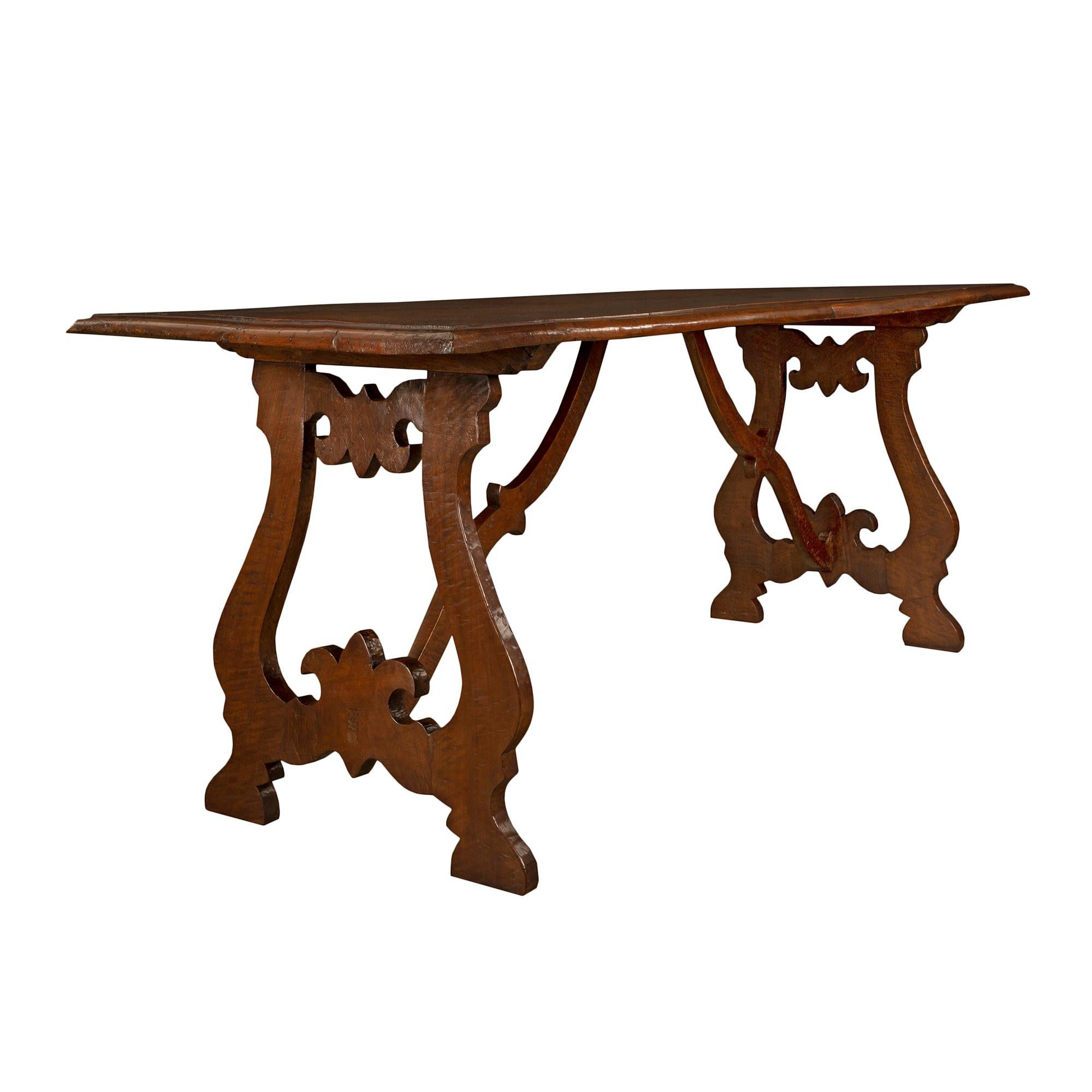 A charming Spanish early 18th century solid walnut trestle table. The table is raised by two pierced scrolled supports, with a Fleur de Lis design at the top and bottom, joined by a scrolled stretcher. The molded solid top is distressed with rounded