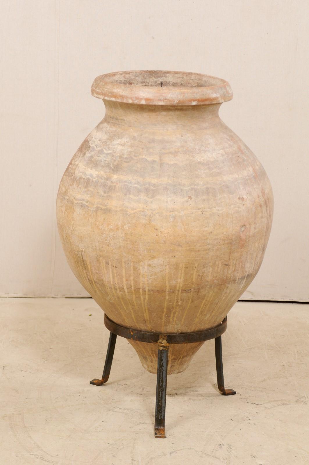 A Spanish large-sized jar from the 19th century on custom stand. This antique vessel from Spain, once used to hold olives, is made of terracotta having a bulbous center, which tapers at the bottom. There is a subtle design pattern and fabulous old