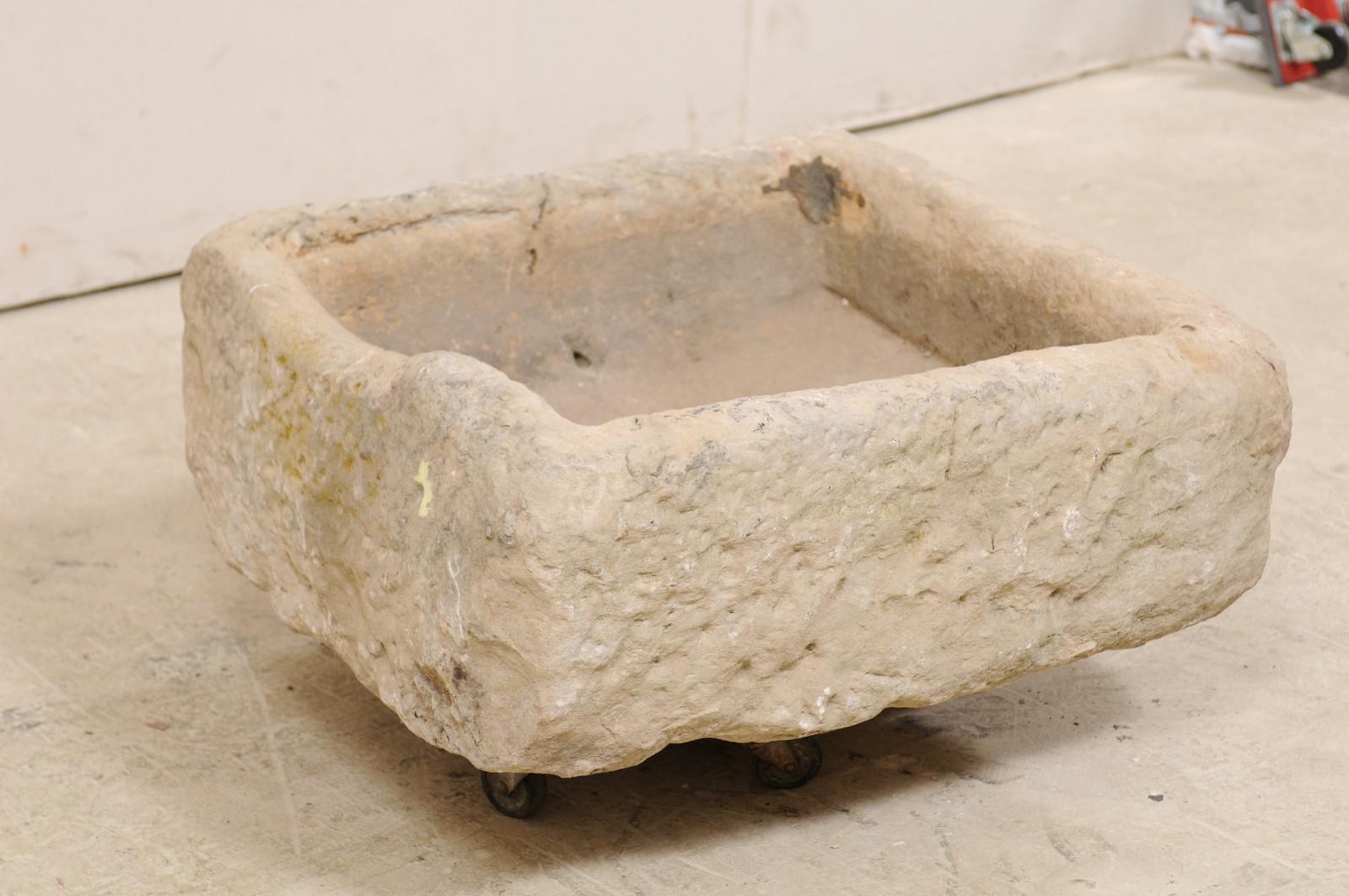 A Spanish square-shaped carved stone basin from the 19th century, potentially older. This antique trough from Spain, has a mostly squared shape which has been hand carved out of a single piece of stone. The basin has a nicely textured surface and