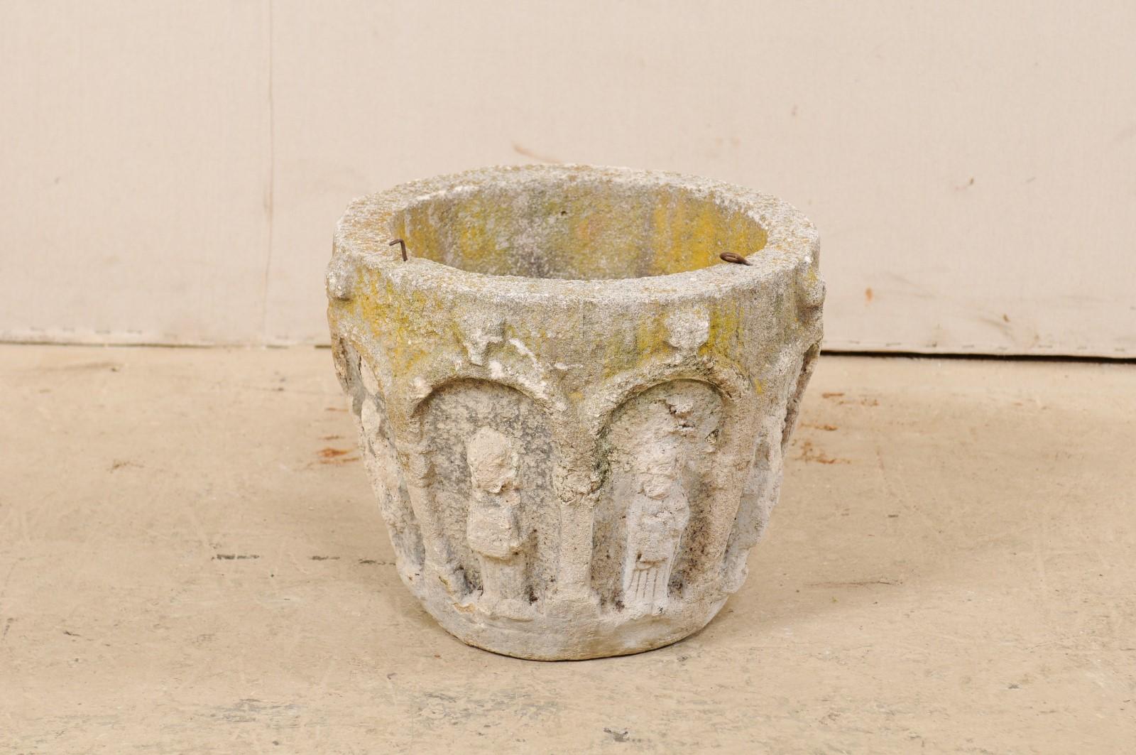 A Spanish cast-stone planter from the early 20th century. This antique planter from Spain was created from cast-stone and artfully decorated about the exterior with various archways and figures within. The round-shaped planter tapers gently and