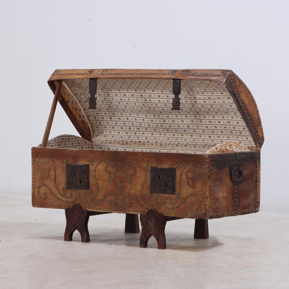 Envuelta en un tono claro de cuero, la decoración de tachuelas metálicas destaca sobre un baúl elevado sobre soportes de madera arqueados de estilo gótico. Quedará de maravilla sobre la mesa de un sofá como escondite para tus tesoros.