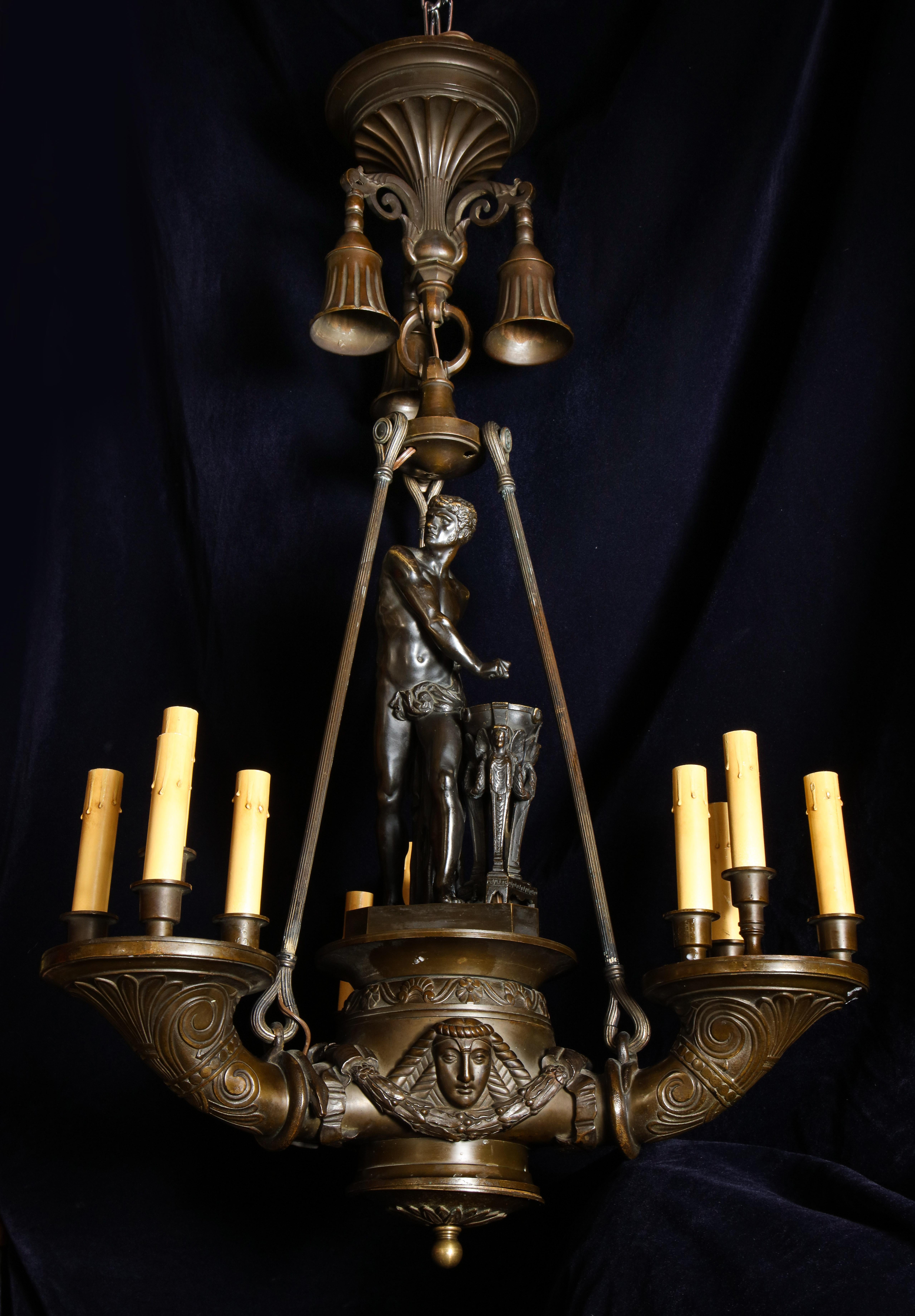 A spectacular and large antique Italian neoclassical patinated bronze multi light figural chandelier of superb detail embellished with a central figure of a neoclassical man and further adorned with neoclassical figural masks.