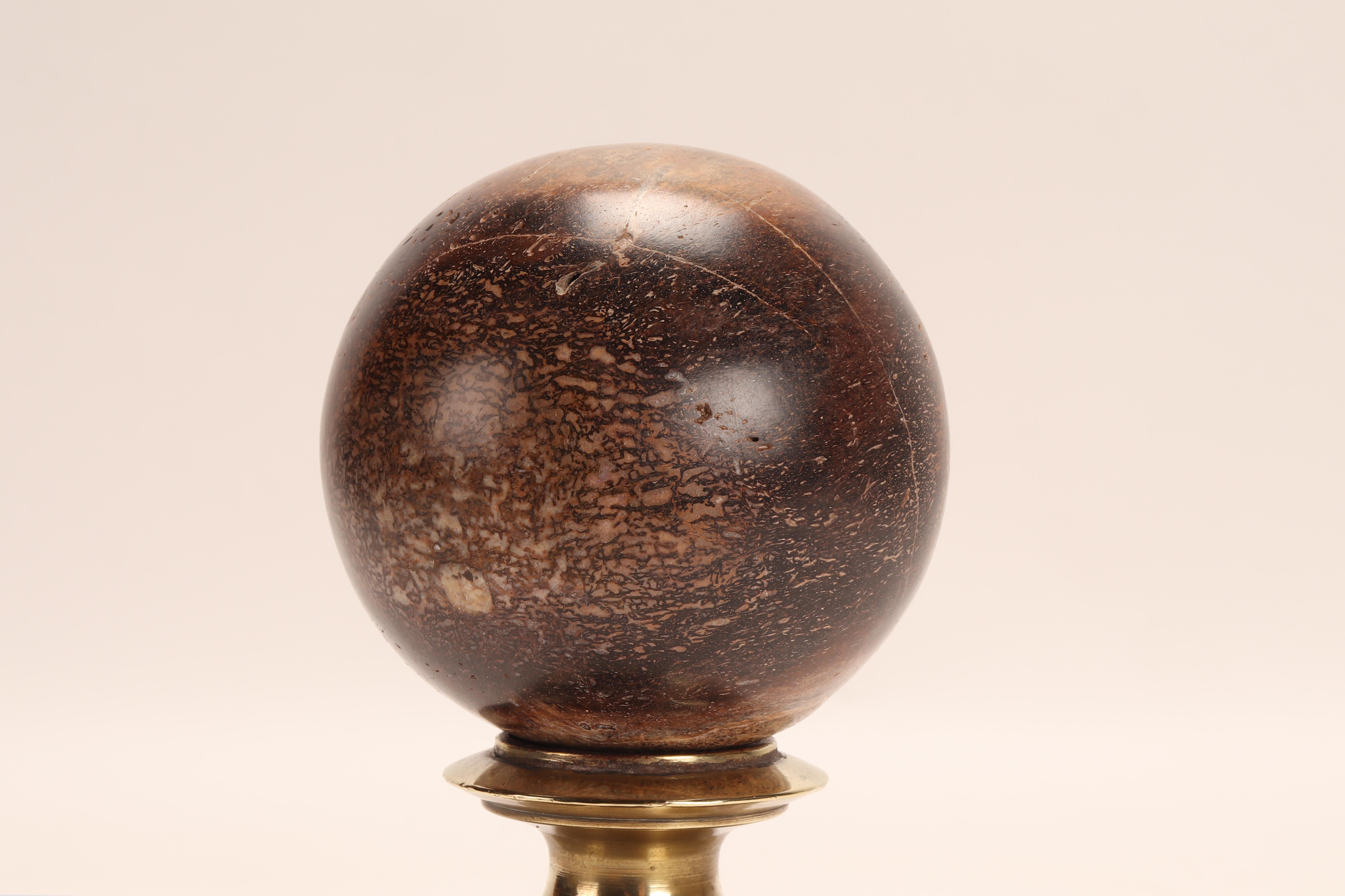A sphere of dinosaur fossil, Plodoco bone, resting on a base, made of brass that has a vase-shaped support with a wavy profile that opens upwards with a concave top. Italy circa 1870.