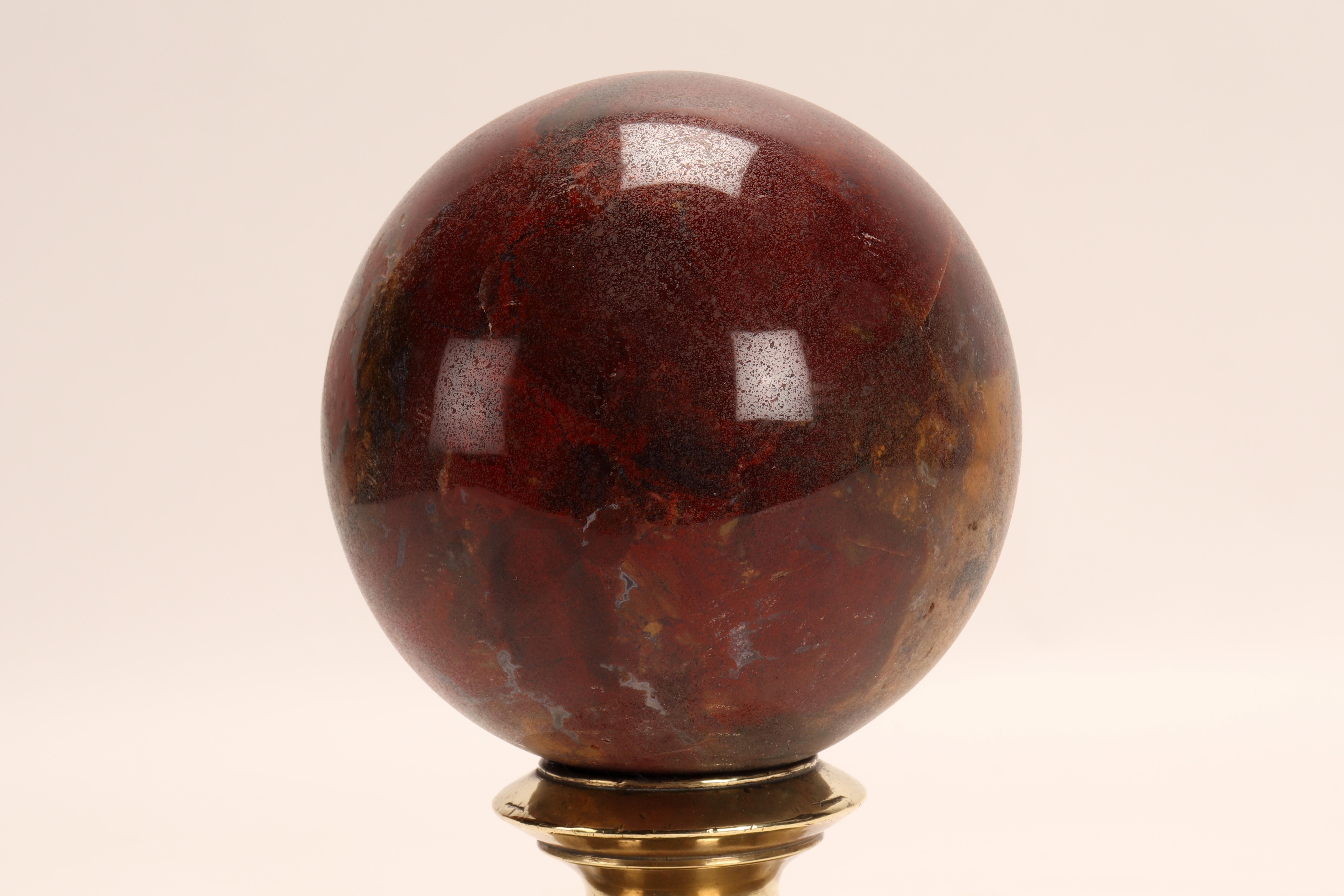 Eine Kugel aus rotem Jaspis, die auf einem Sockel aus Messing ruht. Der Sockel ist vasenförmig und hat ein gewelltes Profil, das sich nach oben mit einer konkaven Spitze öffnet. Italien um 1870.