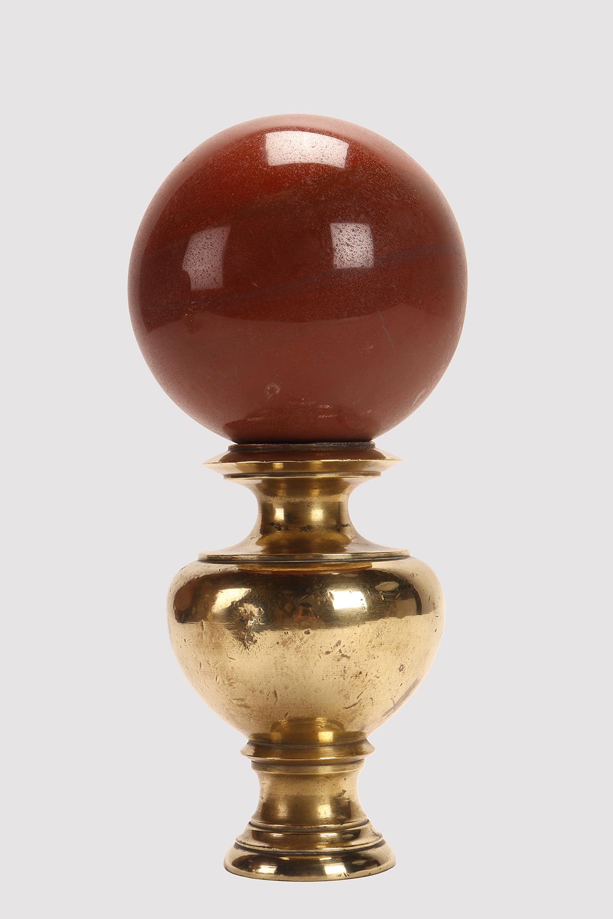 A sphere of red jasper resting on a base, made of brass that has a vase-shaped support with a wavy profile that opens upwards with a concave top. Italy end of 19th century.