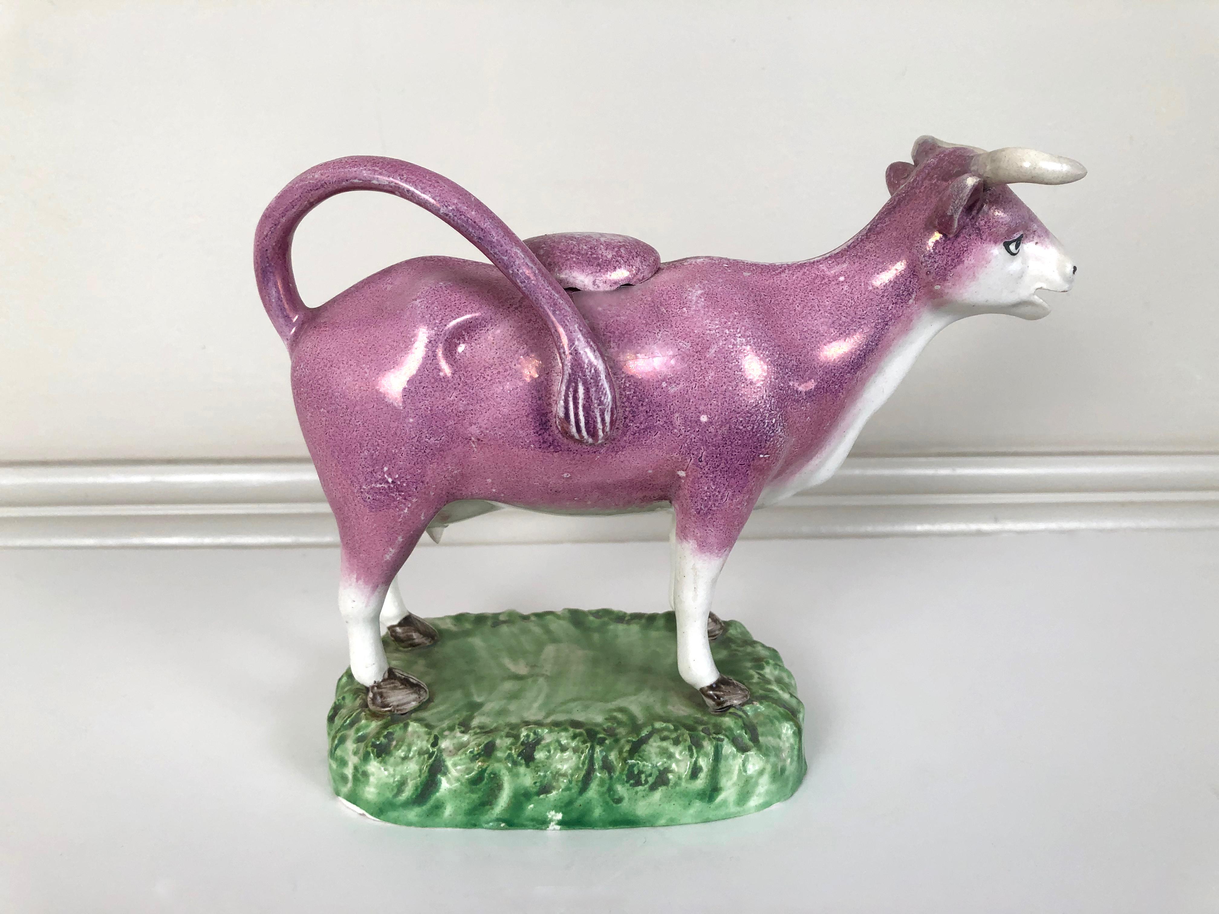 A fine quality Staffordshire pottery pink lustreware cow creamer and cover, modeled as an animated cow, standing with alert, happy expression standing on a green grassy base, English, circa 1820.
