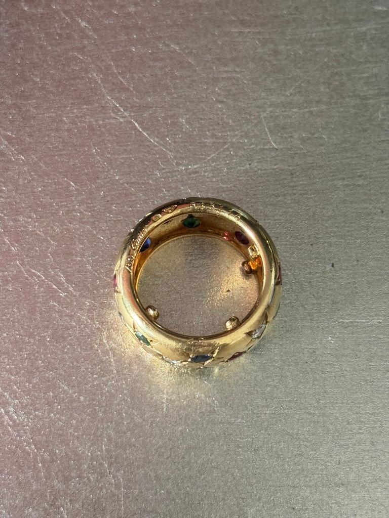 Breites Design, besetzt mit sternförmig angeordneten kreisförmigen Saphiren, Rubinen, Smaragden und Diamanten, montiert in 18K Gold, Gewicht ca: 16 Gramm. 
Signiert Cartier, Frankreich, nummeriert, Prüfzeichen. 
Größe 6.5
