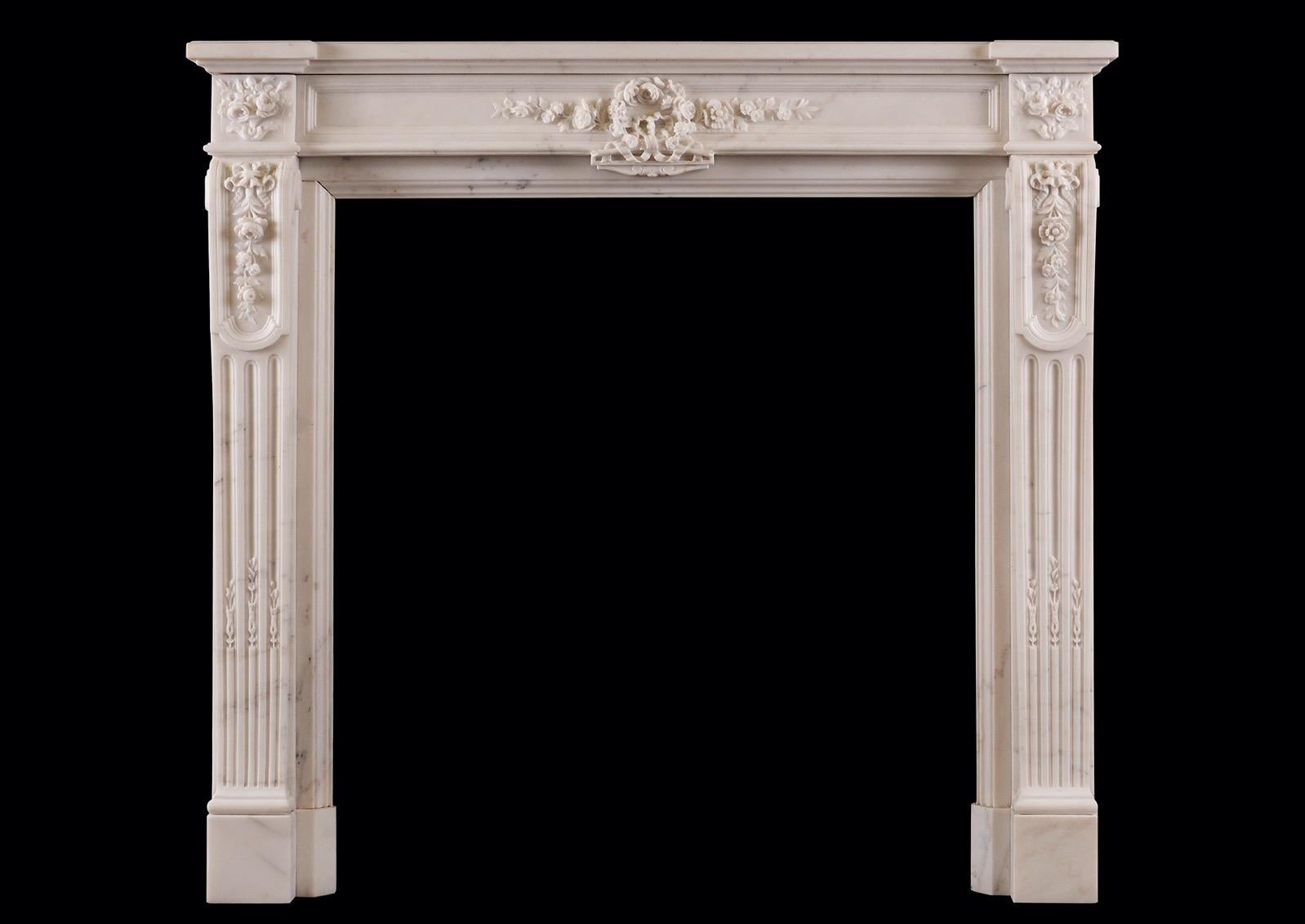 A 19th century French Statuary white marble fireplace in the Louis XVI style. The fluted jabs with carved husks, surmounted by panels carved with ribbons and foliage. The panelled frieze with carved flowers and foliage t centre, flanked by carved