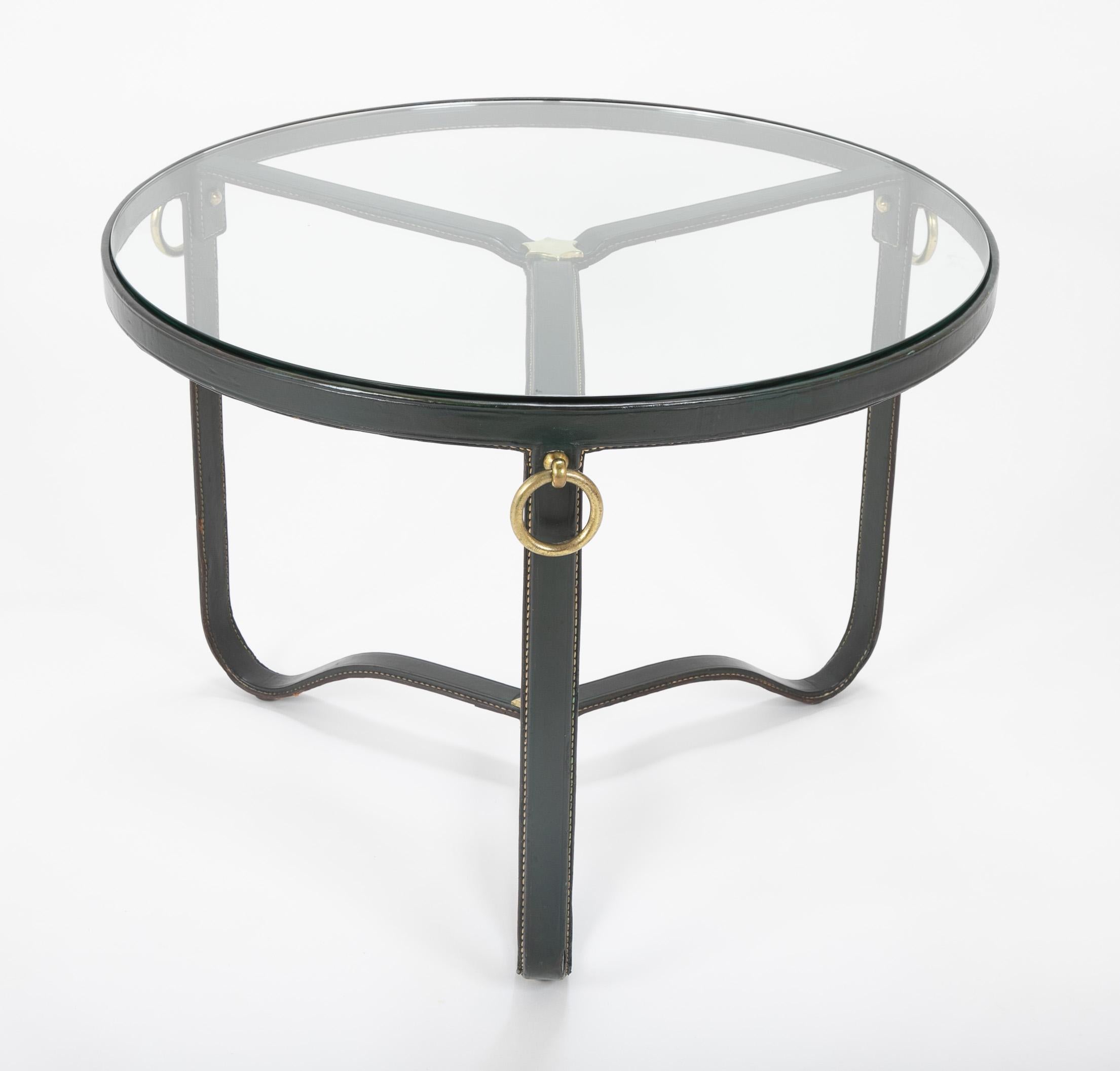 A striking coffee table in steel wrapped with green leather and handstitched designed by Jacques Adnet. Brass rings one match of the three legs along with brass stars at the center of both the upper and lower level. Glass top.
Model illustrated on