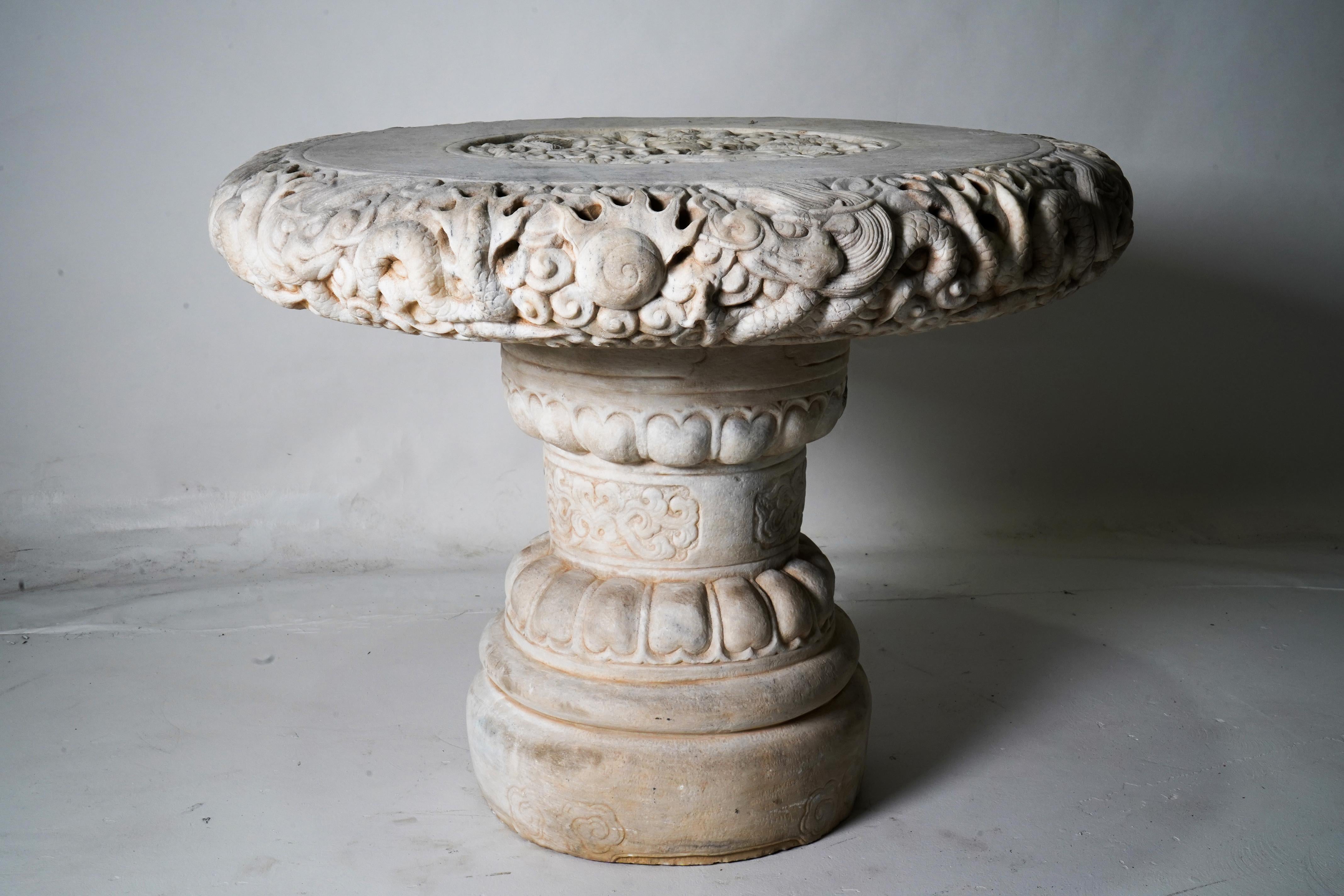 This impressive stone garden table is carved from marble and decorated with writhing dragons. According to Chinese mythology, the dragon sought wisdom. In this rendering, the dragons are seeking a glowing pearl of wisdom. The table comes in two