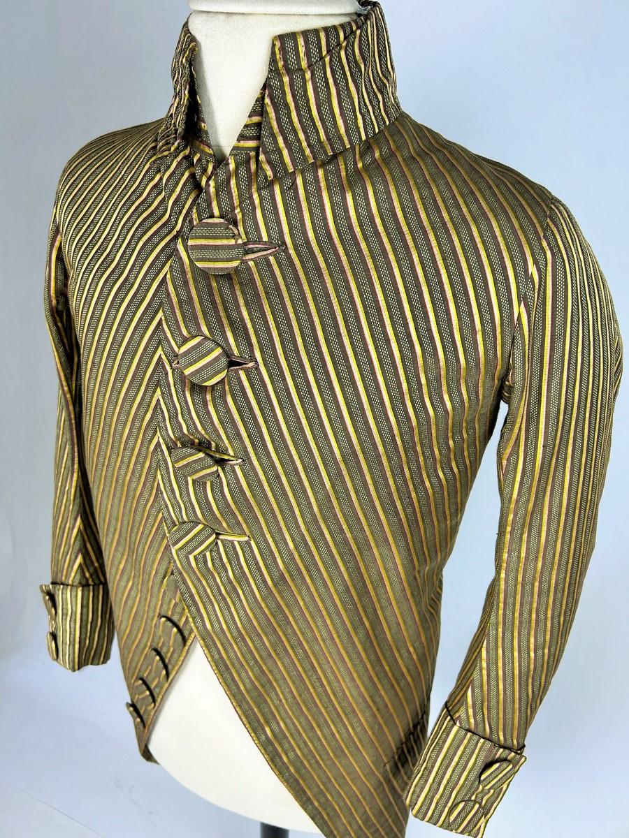 Circa 1785 - 1790
France
Siamoise silk and cotton Habit or frock coat with fine tricolour, speckled and shaded stripes dating from the French Revolution. Fitted, scooped front and pleated tail. High officer's collar with turned-down panels and long