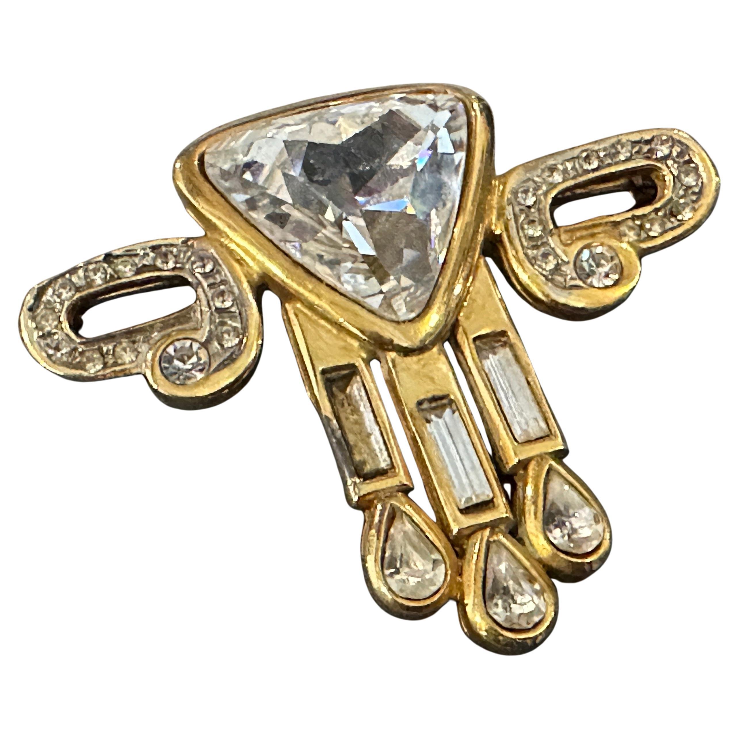 Diese Brosche ist ein atemberaubendes Beispiel für Art-Déco-Modeschmuck der 1930er Jahre, der sich durch seine geometrischen Formen, seine Symmetrie und seine luxuriöse Ästhetik auszeichnet. Ein markanter Stein im Dreiecksschliff, wahrscheinlich ein