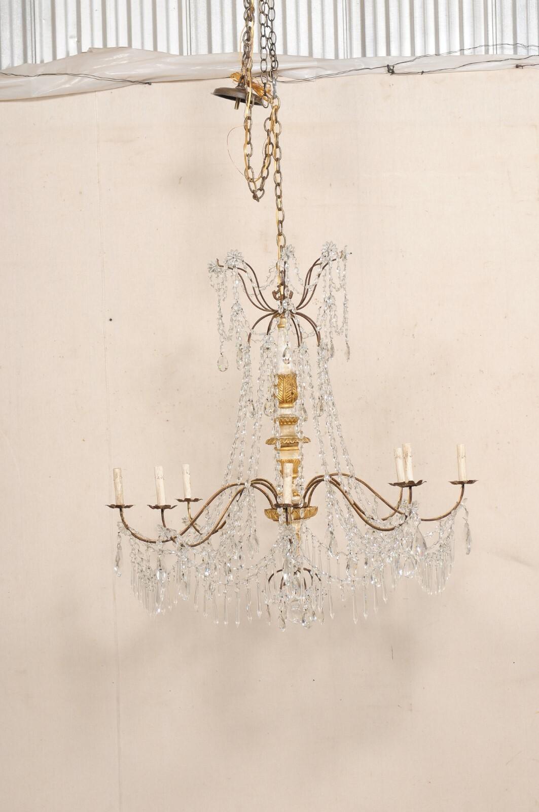 An Italian crystal and gilt wood column chandelier from the 19th century. This antique chandelier from Italy features an elegantly carved wood central column with gilt finish, decorated with a collection of various crystals, swagged Italian glass