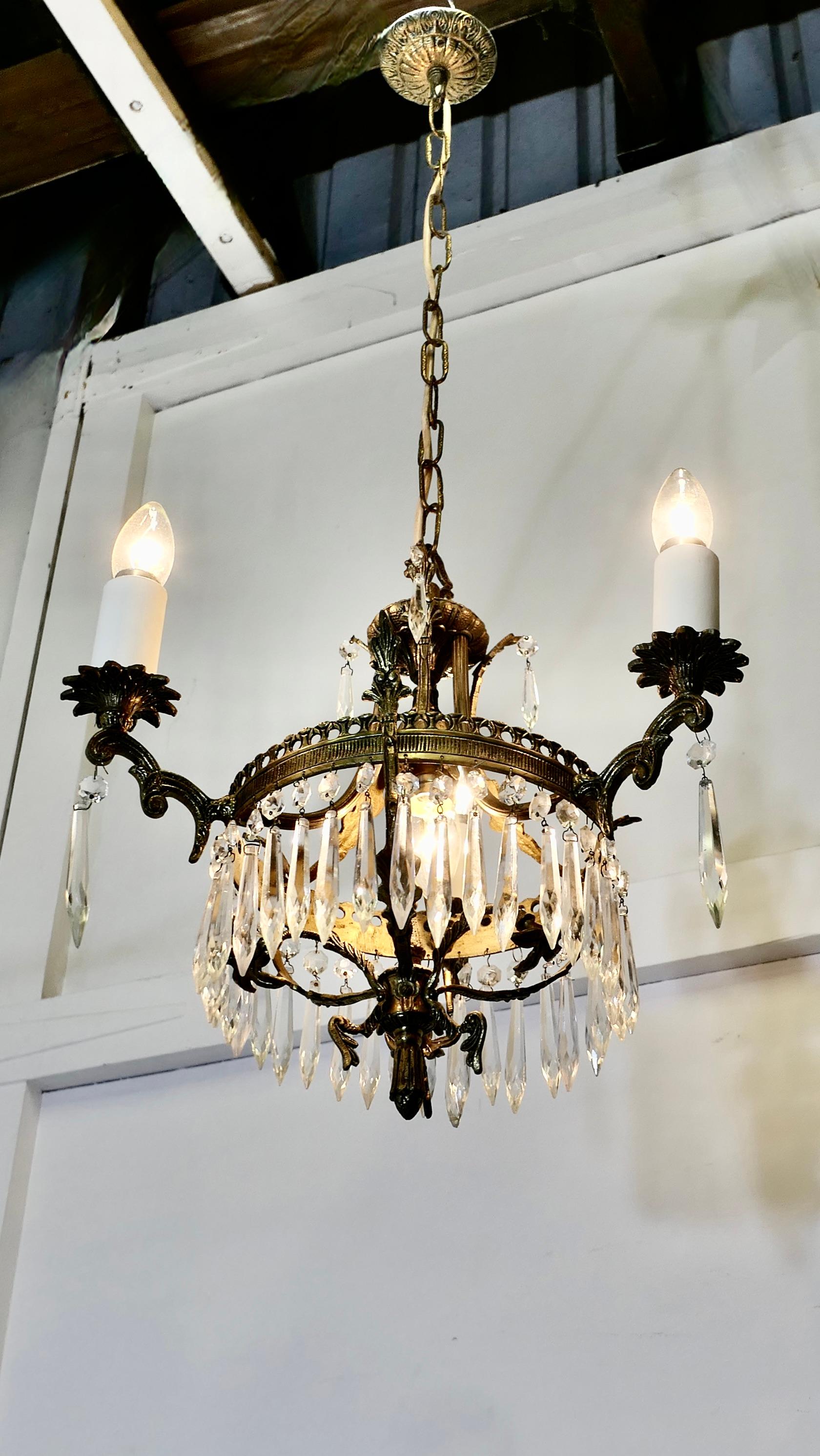 A Stunning 3 Branch Brass and Crystal Chandelier 

This is an excellent quality piece, it has a brass crown hung with crystal drops in the centre this has 3 branches supporting brass sconces and a centre bulb which lights up a brass floral centre