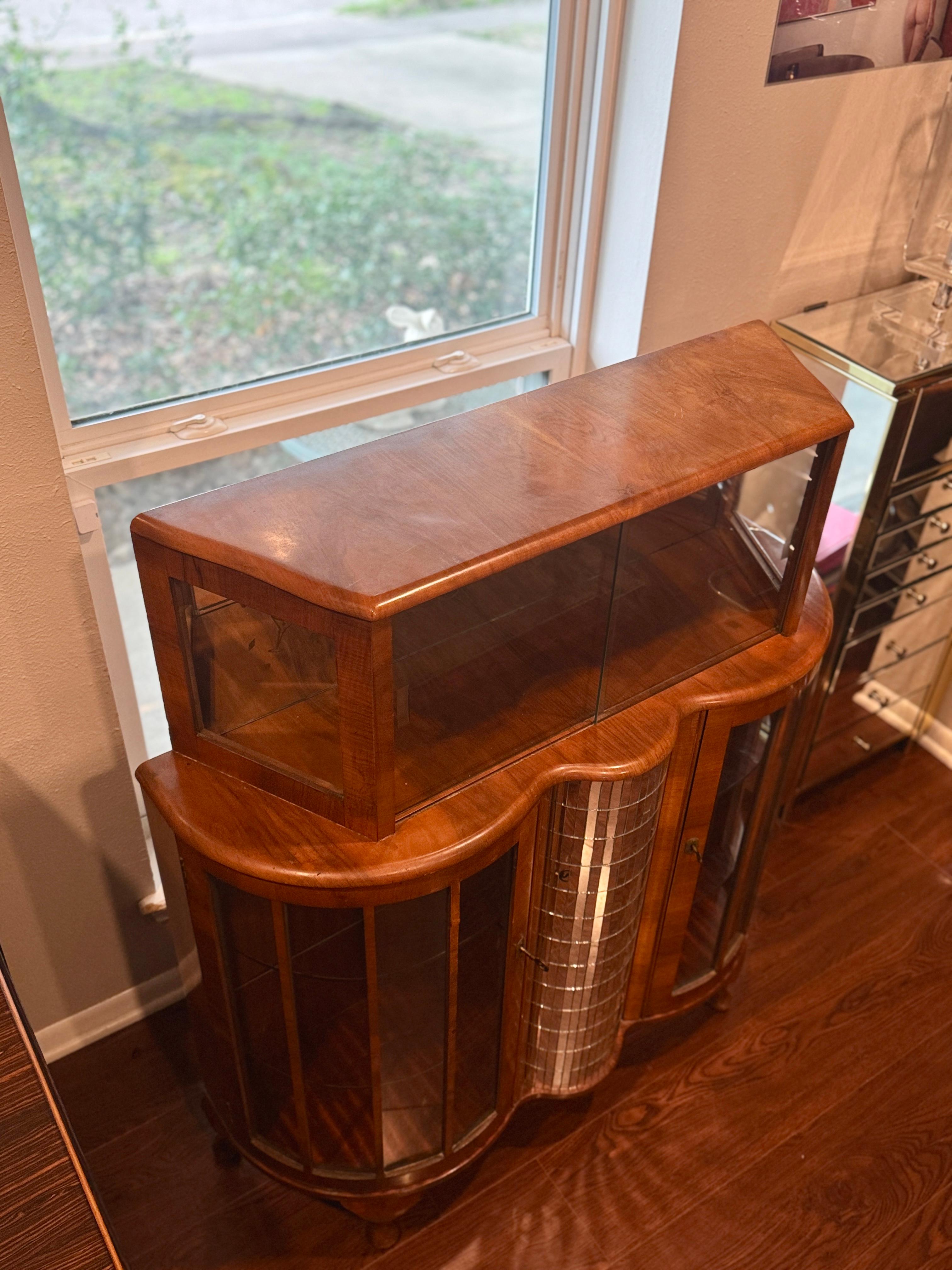 Uno splendido mobile da cocktail in stile Art Déco, risalente agli anni '30 circa. Questo bellissimo pezzo ha una finitura impiallacciata in mogano e poggia su gambe cabriole. La parte anteriore a serpentina è dotata di due porte con serratura in