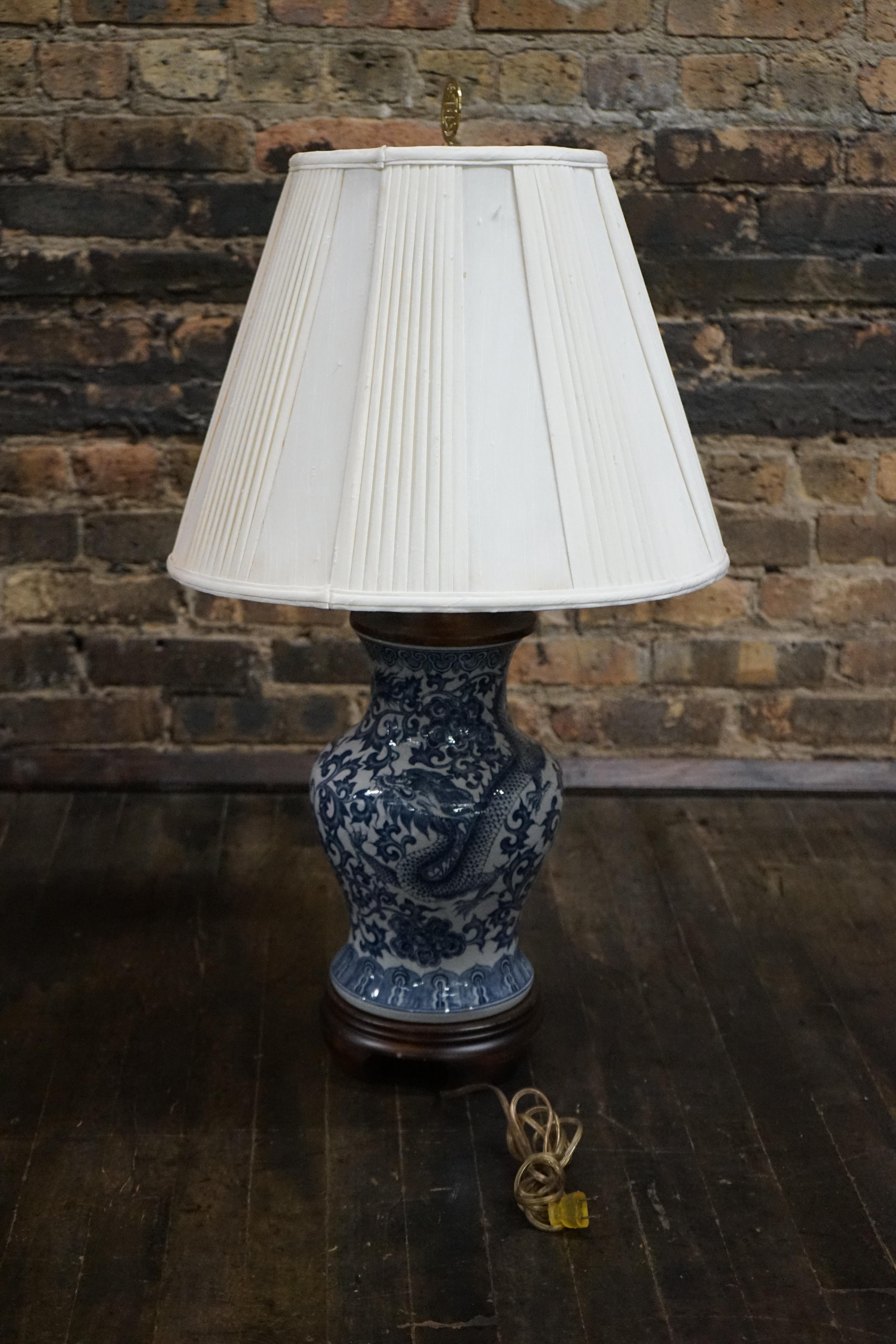Beautiful blue and white ginger jar style lamp by Frederick Cooper.  The lamp has an Asian motif painted in the body and it features a dragon.  The painting is in blue.  The body of the lamp is an antique white.  The base is dark wood.  There is a