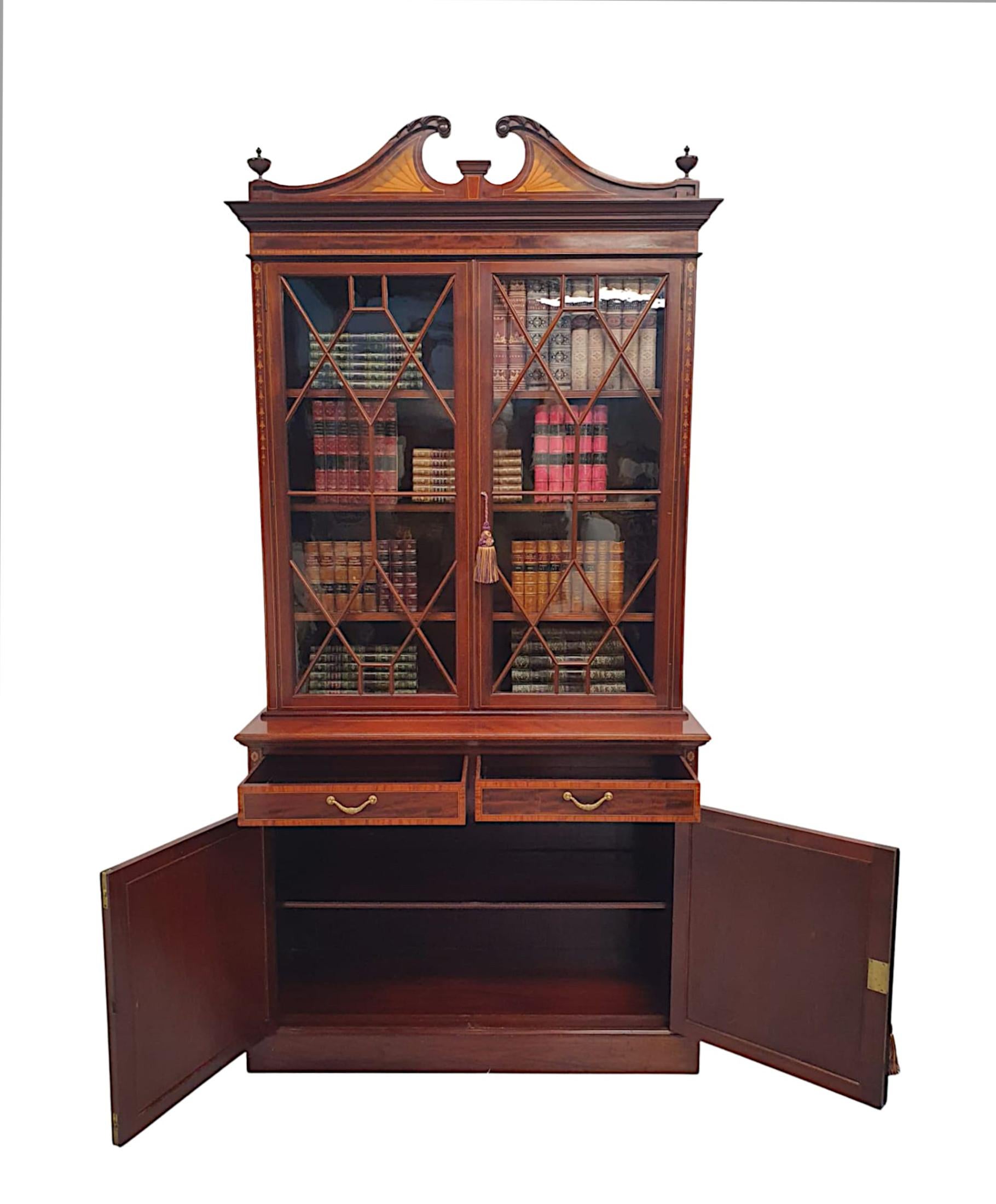 A stunning Edwardian mahogany two door bookcase, of fabulous quality, finely carved with rich patination, fine grain, line inlaid and crossbanded with fabulous marquetry detail throughout. The broken swan neck pediment gorgeous scrolling acanthus