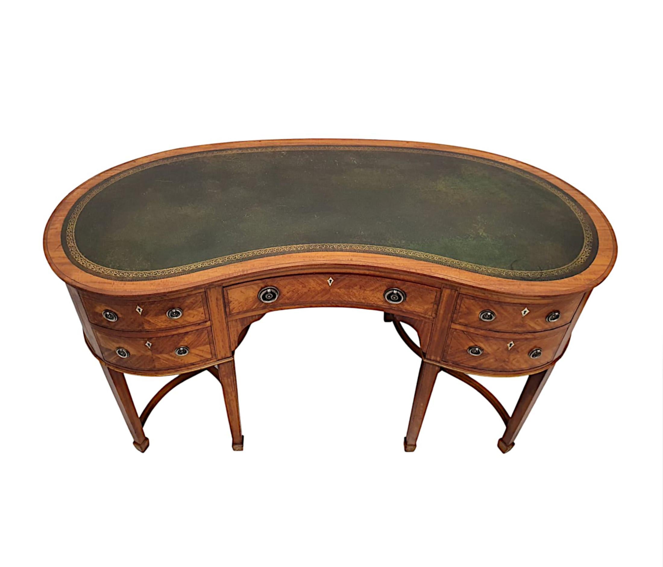 A stunning Edwardian satinwood kidney shaped desk, of fabulous quality, finely carved and line inlaid throughout. The moulded desk top is fitted with a gorgeous green gilt embossed tooled leather writing skiver surface above frieze fitted with