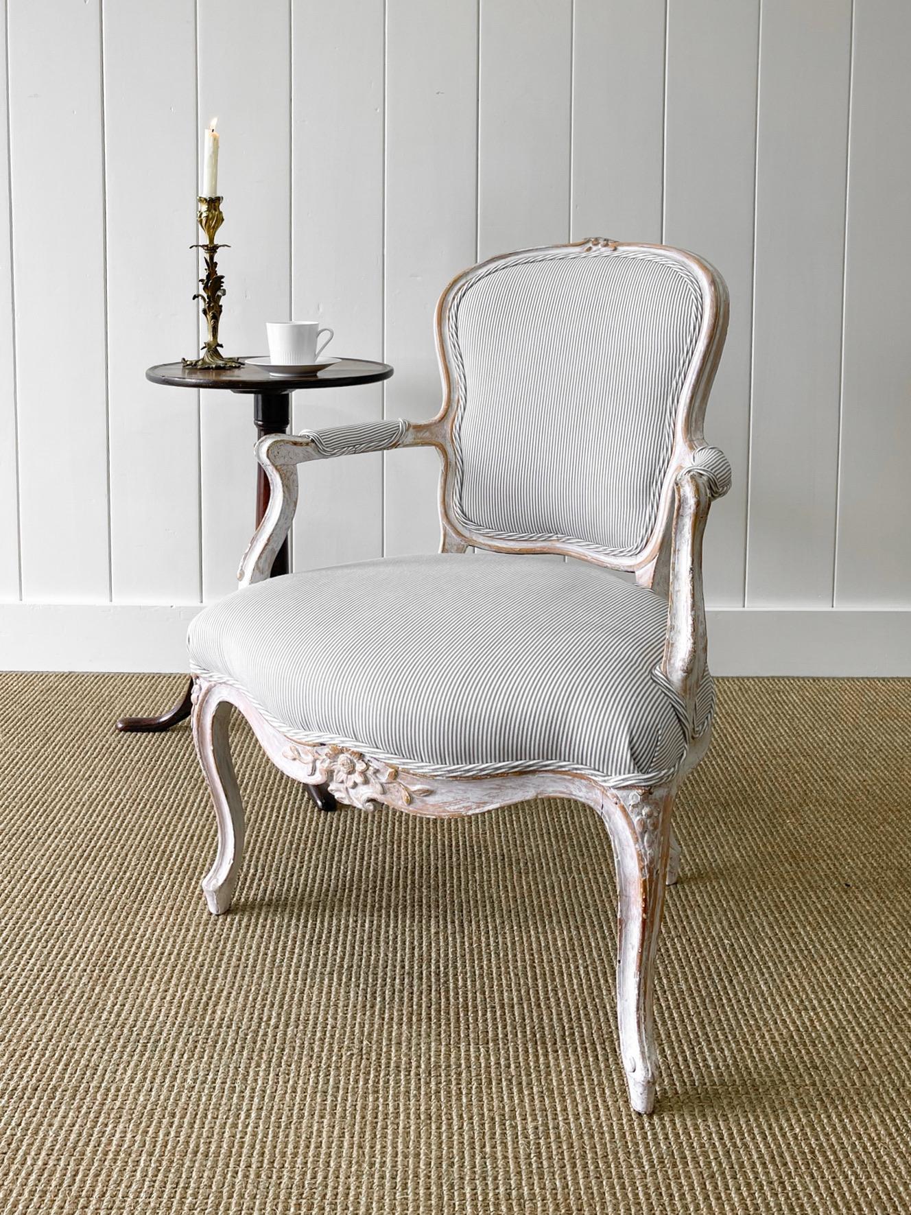A stunning French 18th century fauteuil arm chair. Newly upholstered in a Kravet ticking 100% linen fabric. A very good patina on this chair! Excellent old white paint with hints of original gold gilding. Exquisite carving. The silhouette is