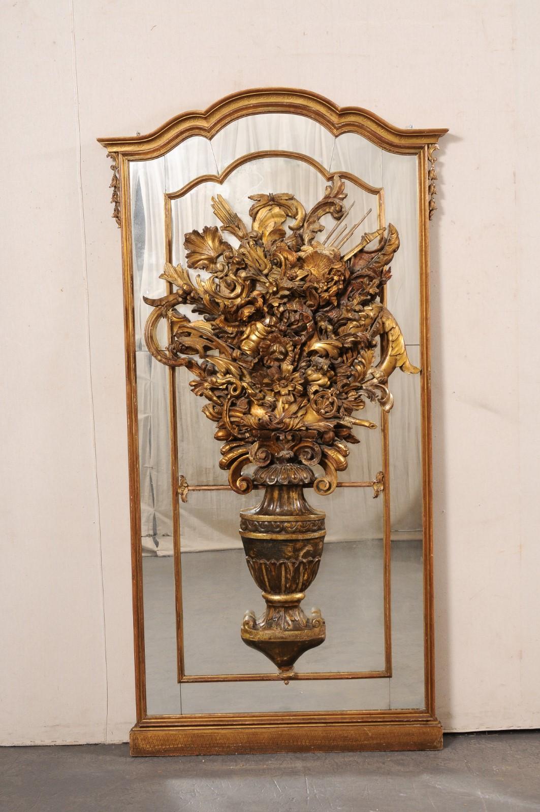 An Italian large-sized elaborate floor mirror from the 19th century. This antique mirror from Italy features a elaborately carved Neoclassical carved-wood urn, located atop the mirror at center, with bouquet abundantly filled with various foliage,