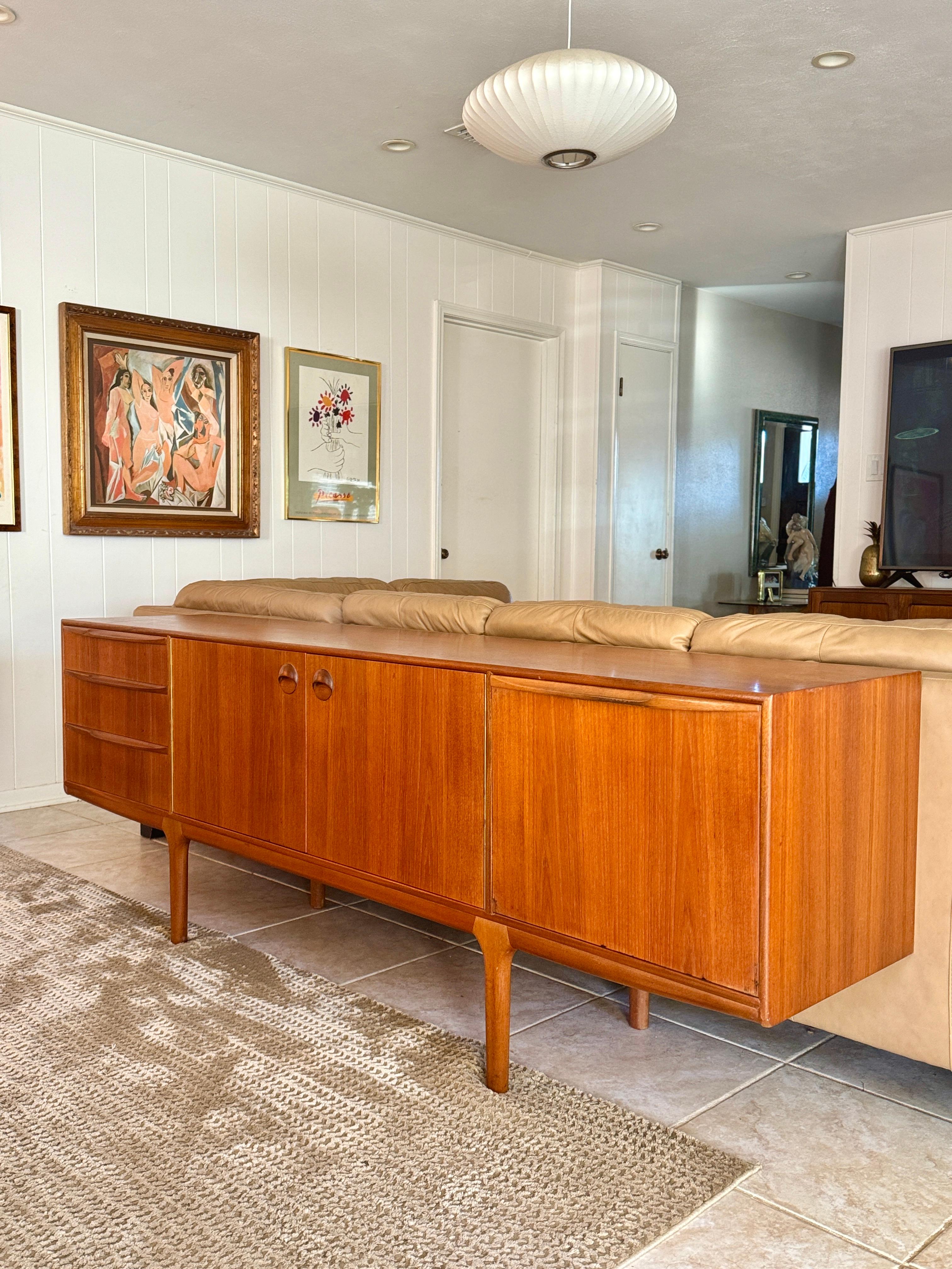 A stunning mid century modern sideboard by renowned Scottish furniture maker McIntosh, circa 1960s. This is the sought after “Dunfermline” model, featuring the brand’s signature folded handles and a sleek pull out tray for added functionality.