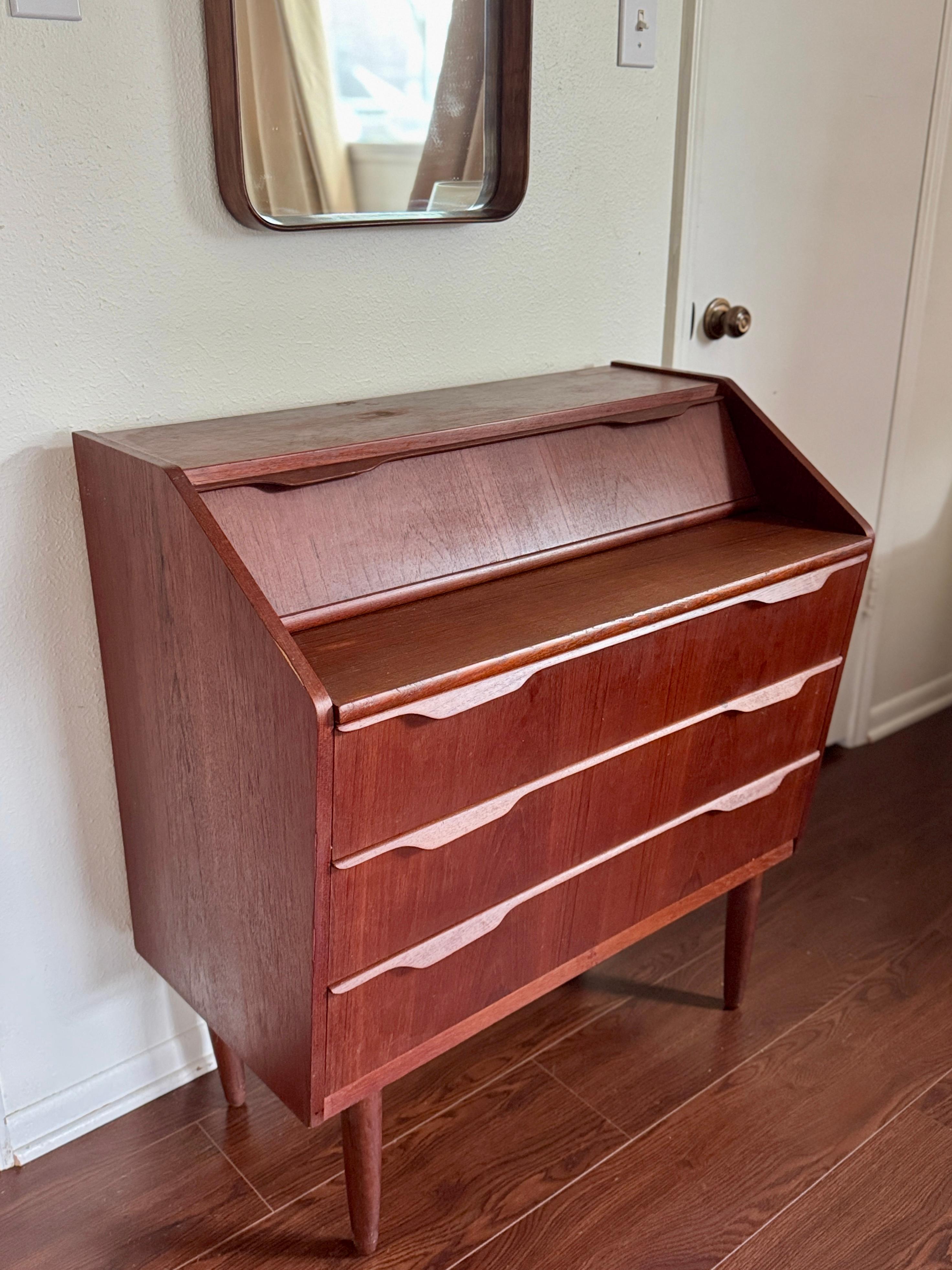 A stunning mid century modern teak secretary desk made in Denmark, circa 1960s. Crafted by renowned maker CENTURY, this piece features clean lines, a darker warm teak grain, and timeless Danish design. A large extendable pull out desk creates a