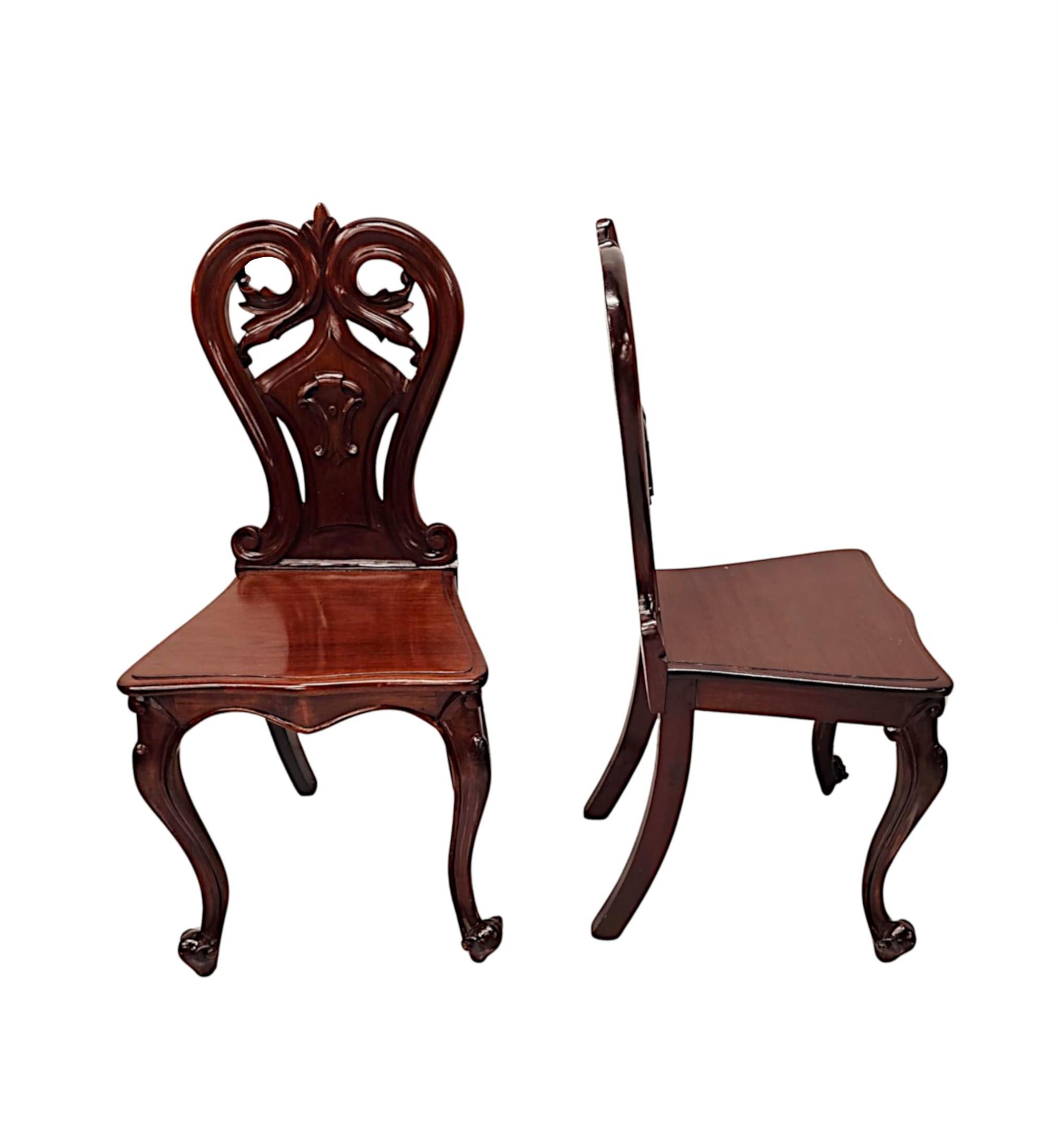 A stunning pair of 19th Century well figured, mahogany hall chairs, finely hand carved with gorgeously rich patination and grain.  The shaped and pierced shield back with exquisite motifs comprising of beautiful scroll detail to the central reserve