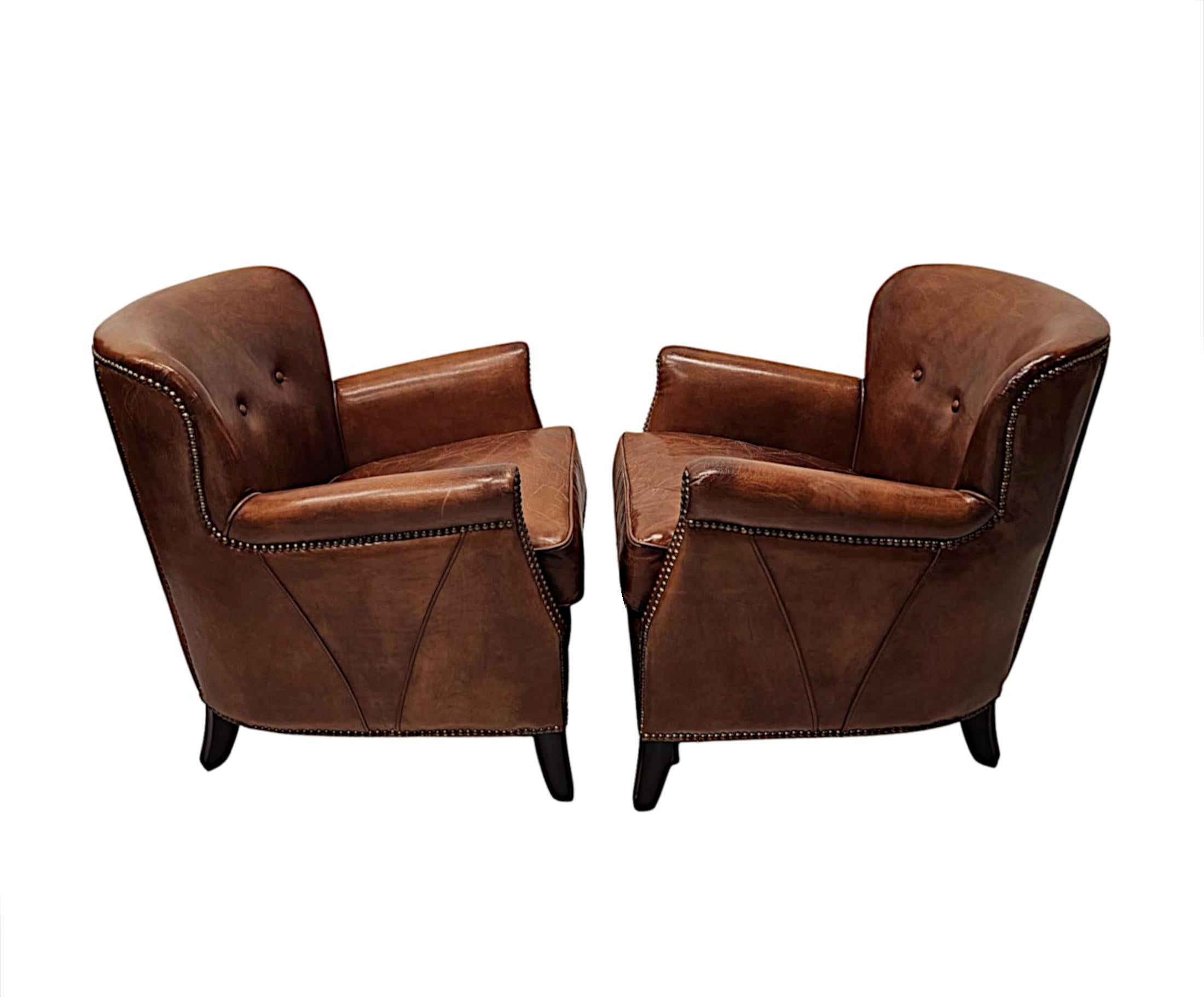 A stunning pair of club armchairs in the Art Deco style of neat proportions, fabulous quality and upholstered in gorgeously rich elegant brown leather with decorative brass studding and piping detail throughout.  The cushioned and shaped button back