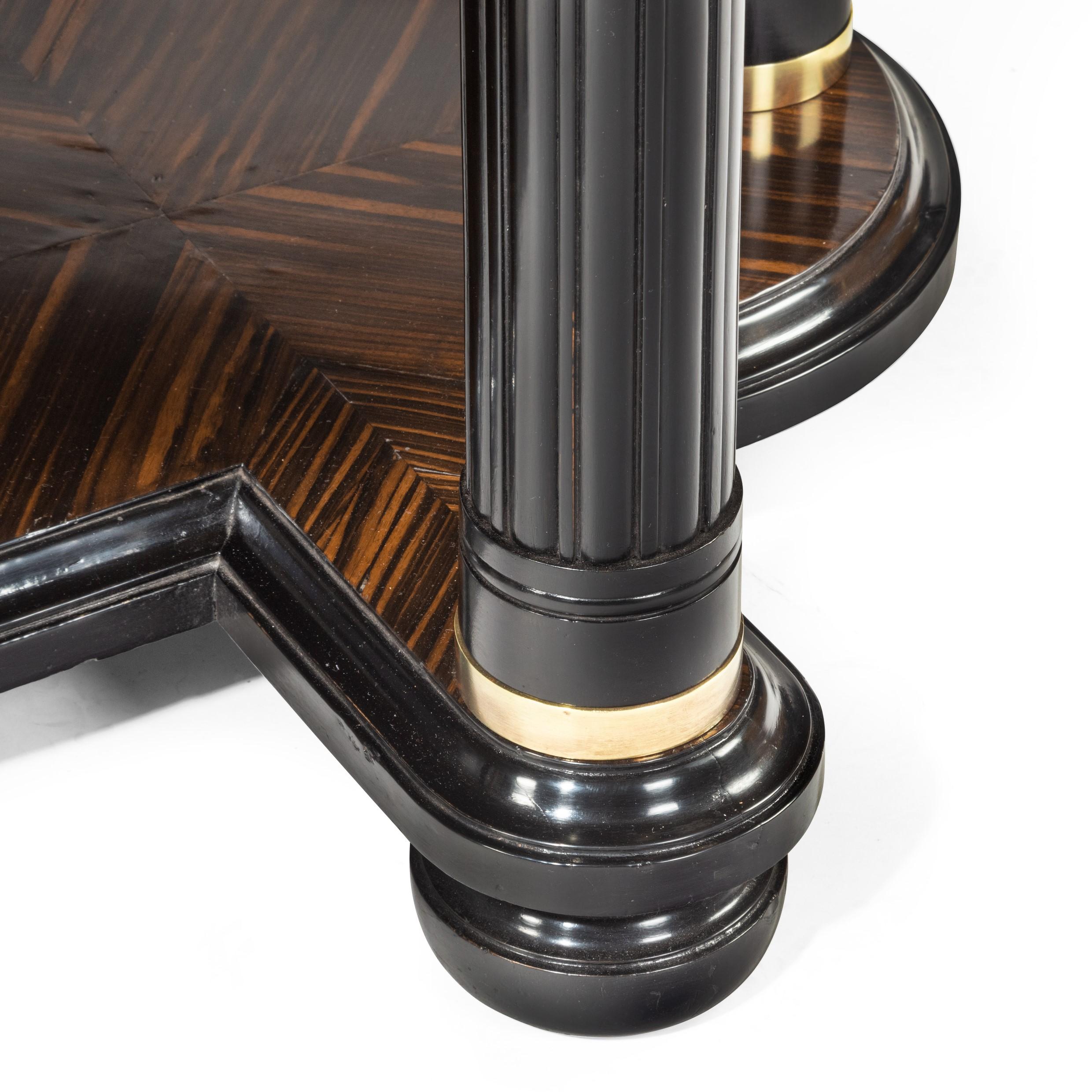 A stylish Art Deco zebra wood centre or dining table, the top and solid stretcher with rounded ends below both decorated with dramatic quarter veneers with a central diamond, the frieze with chevrons and plain brass edging, all set upon six reeded