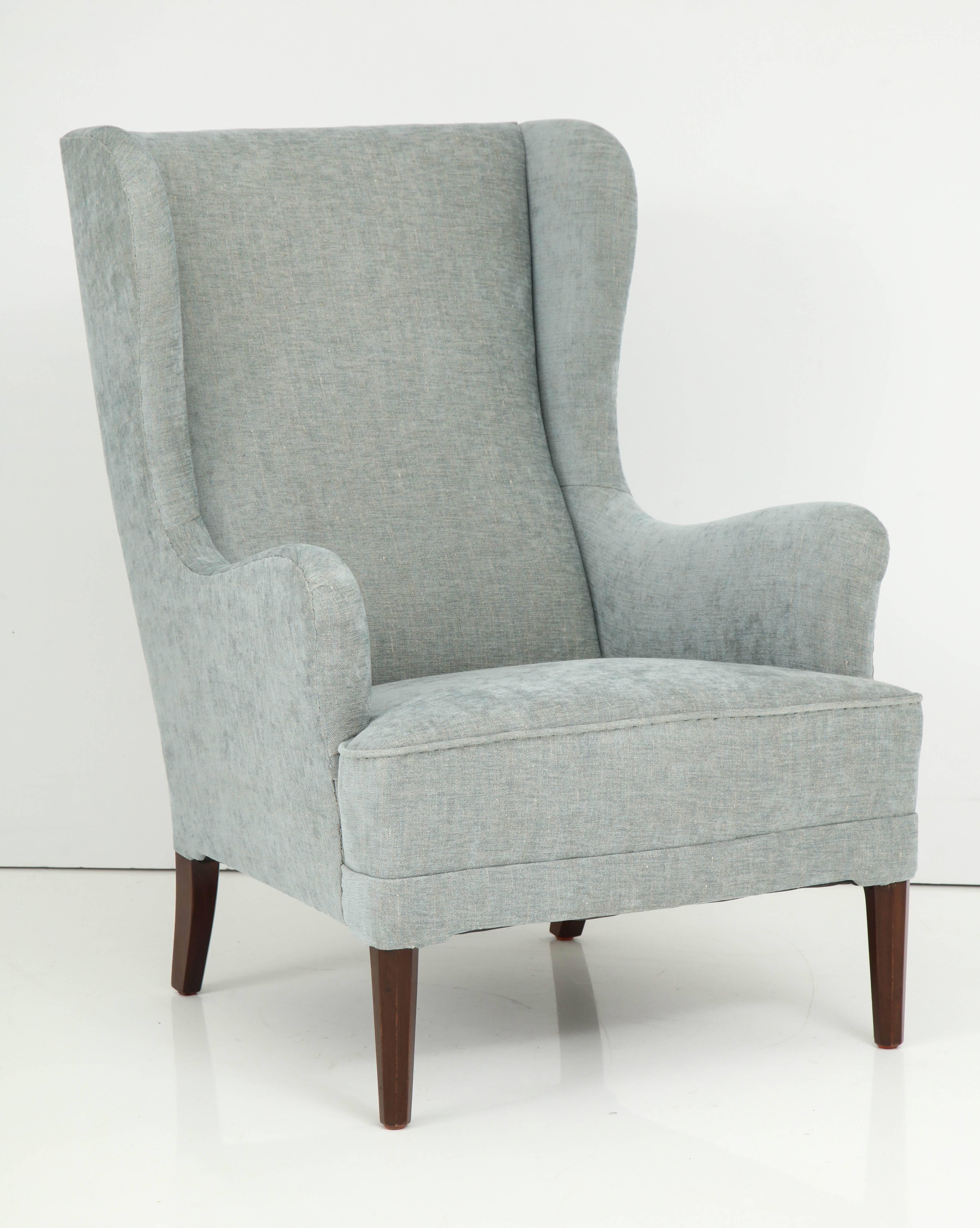 A Danish upholstered wingback armchair with stained beechwood legs and an associated footstool, circa 1940s. New upholstery

Measurements do not include footstool.