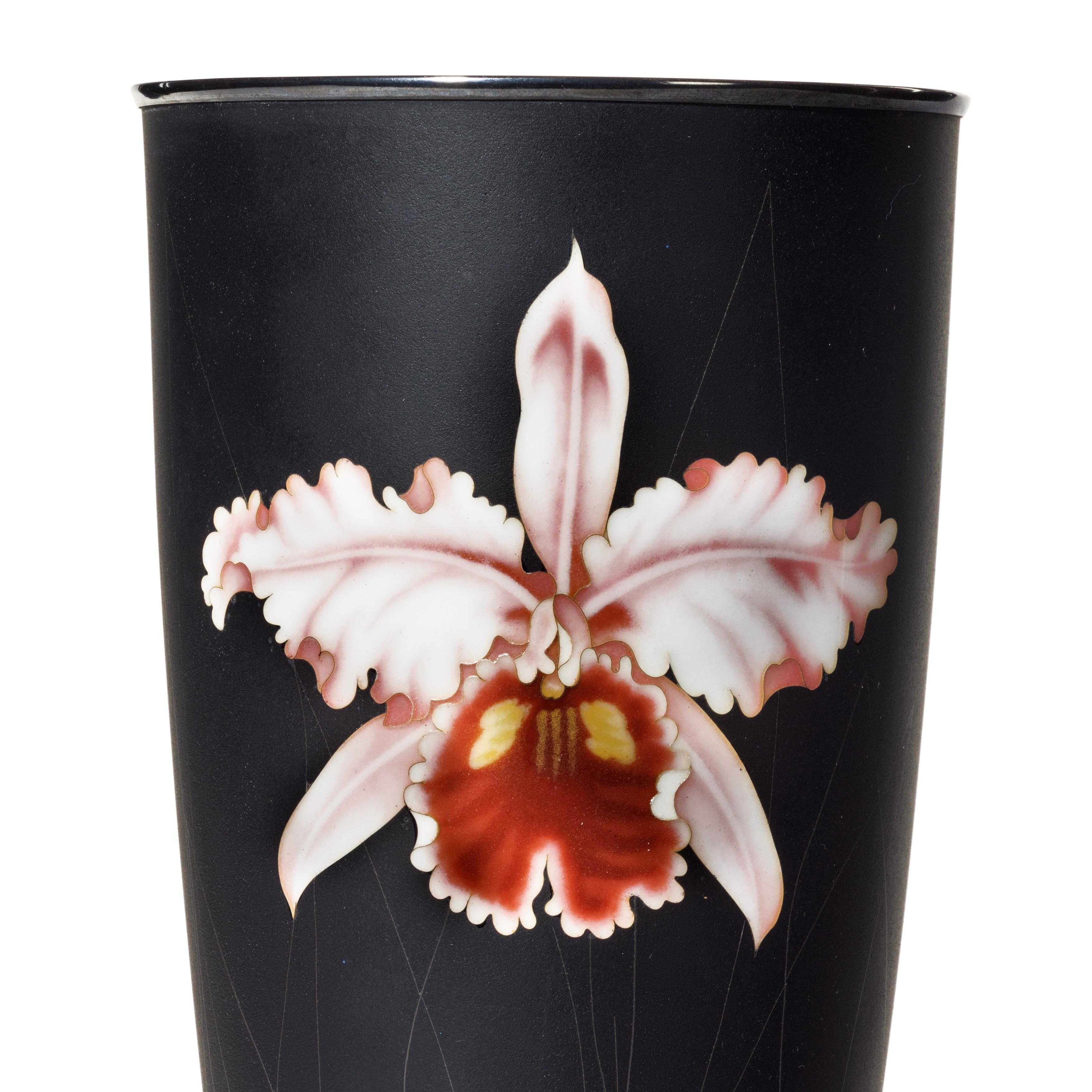 Eine stilvolle Cloisonné-Emaille-Becher-Vase von Ando aus der Showa-Periode mit einer einzelnen rosafarbenen Orchidee auf mattschwarzem Grund, mit der Ando-Drahtmarke im Sockel und gestempelten Silberbeschlägen.  Japanisch, um 1950.

Höhe 10 Zoll