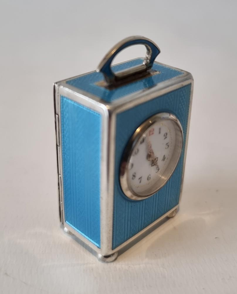 A superb sub miniature silver and light blue guilloche enamel carriage or boudoir clock by Juvenia, in leather carry case. The superb engine turned enamel, which is even applied to both sides of the handle. White enamel dial with arabic numerals and