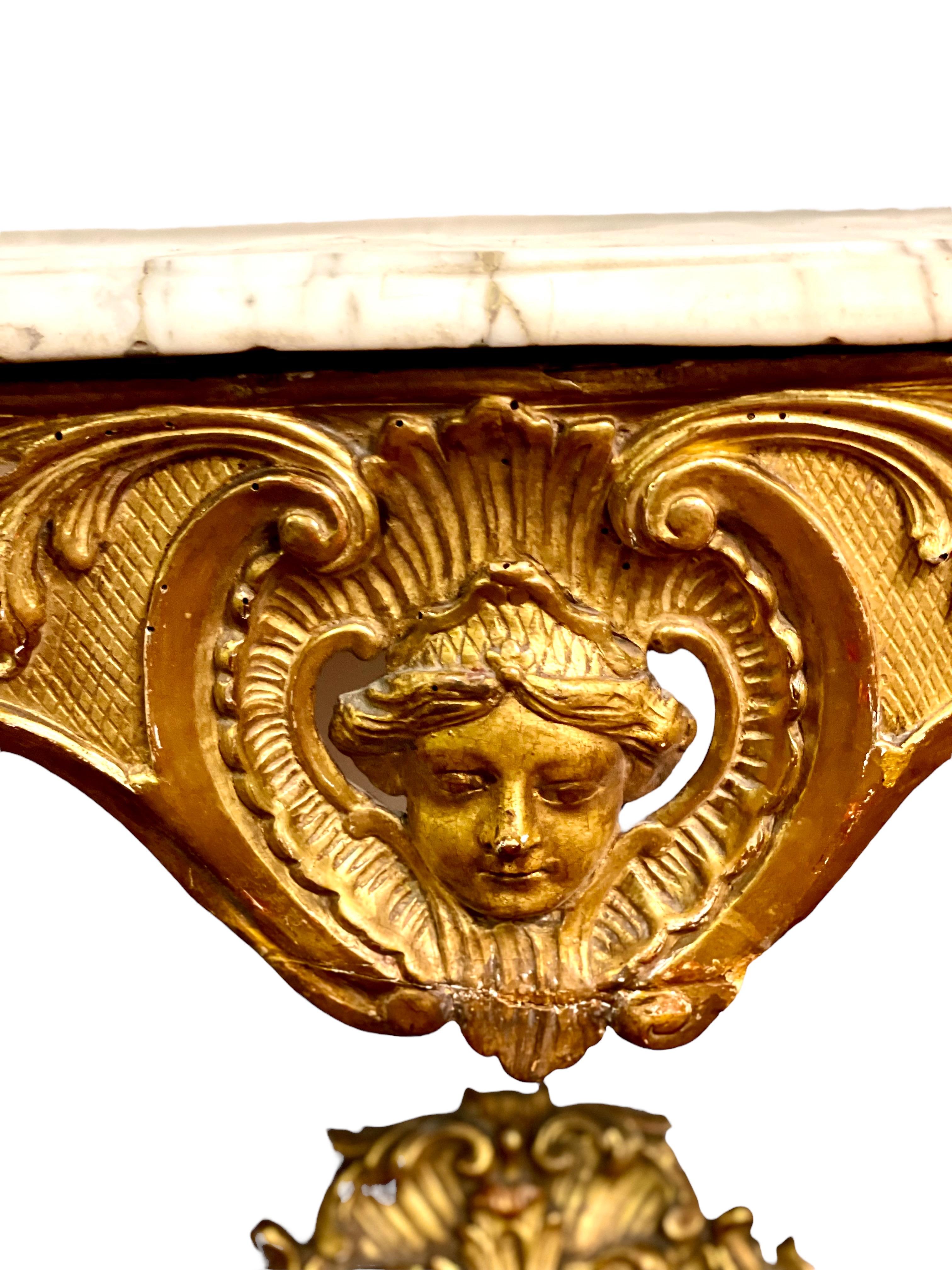 This rather elegant and unusual, ornately carved giltwood Louis XV console table features two arching legs connected by an openwork crosspiece embellished with motifs of shells and foliage surrounding a gleaming, angelic face.           
    The