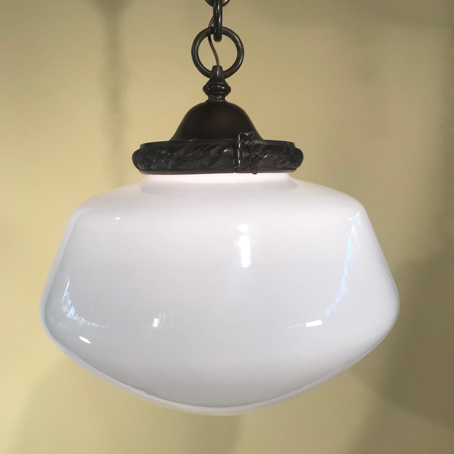 A 1920s bronze pendant light with a large white opal glass globe. The bronze fitter has a dark antique patina and is cast with decorated wreath and ribbon design, supported by a large loop, heavy decorative chain and original bell -shaped ceiling